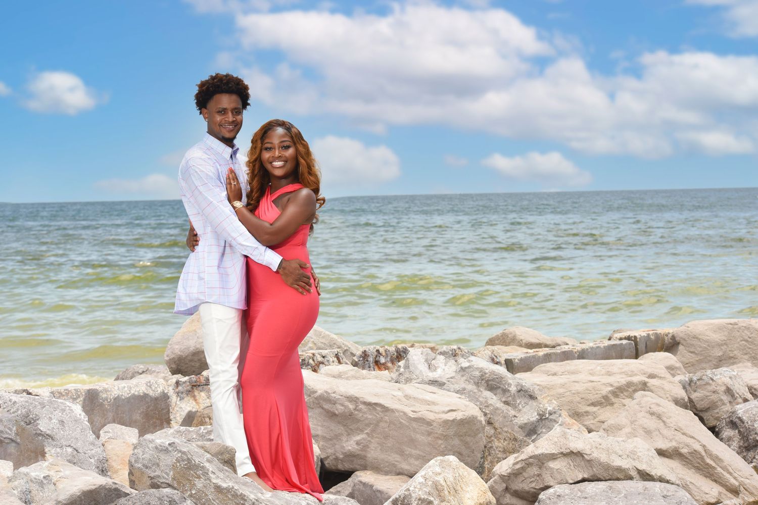 Romantic beach photoshoot with rocky coastline and blue water backdrop.