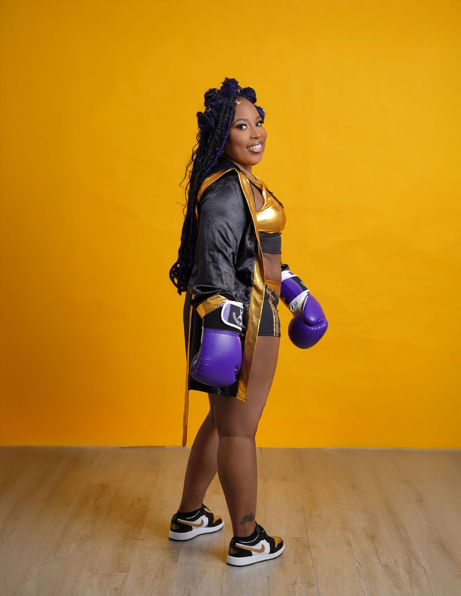 Person in boxing attire performing squats against a vibrant yellow wall with purple dumbbells in Tampa Florida.