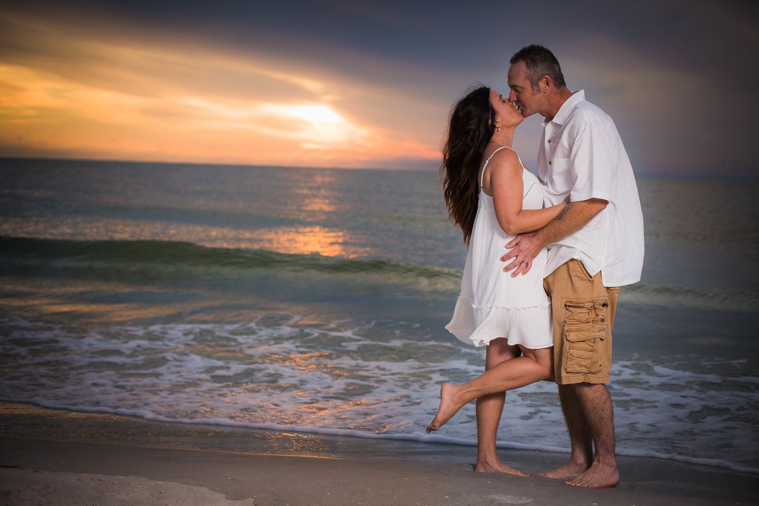 Silhouettes of a couple embracing on the beach during a dramatic orange sunset over the ocean.