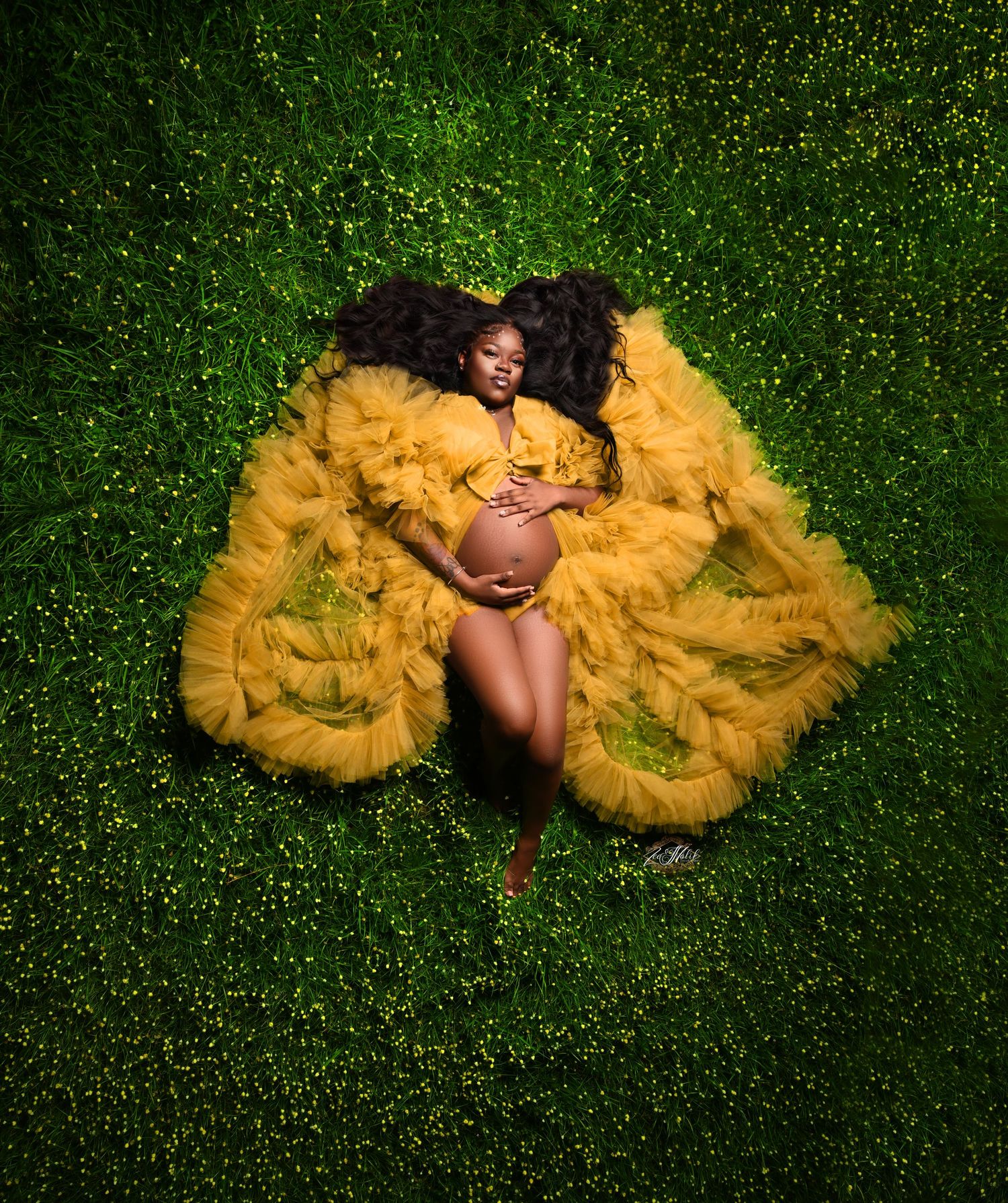Maternity photo featuring a yellow tulle dress against vibrant green grass background.