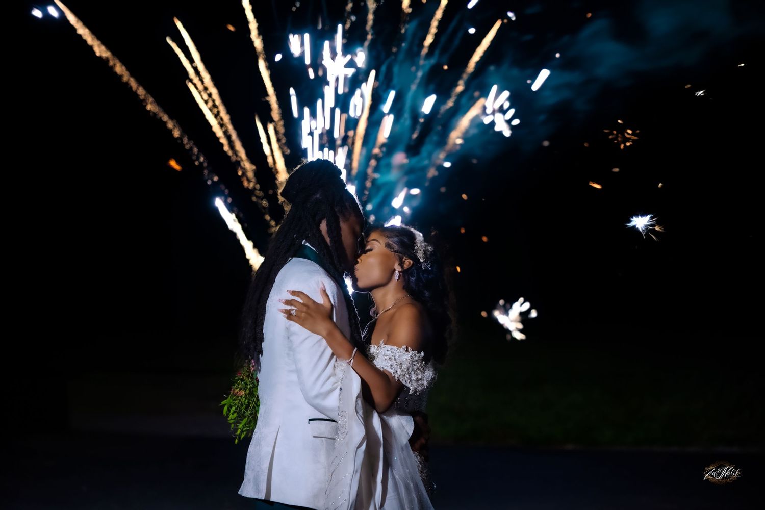 Wedding couple poses against night sky with fireworks creating magical sparkles in the background.