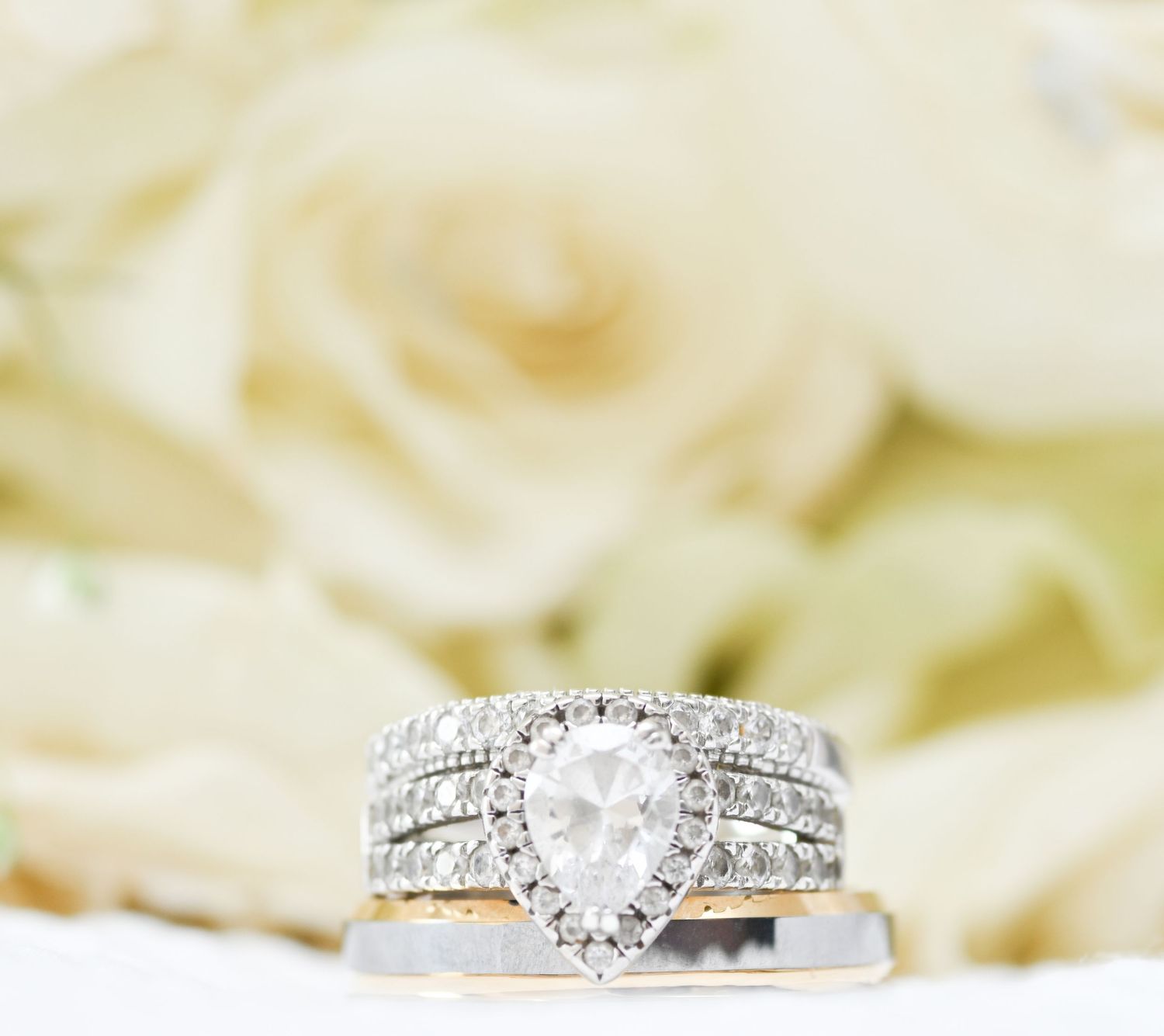 Close-up of elegant diamond engagement rings with white roses in the background.