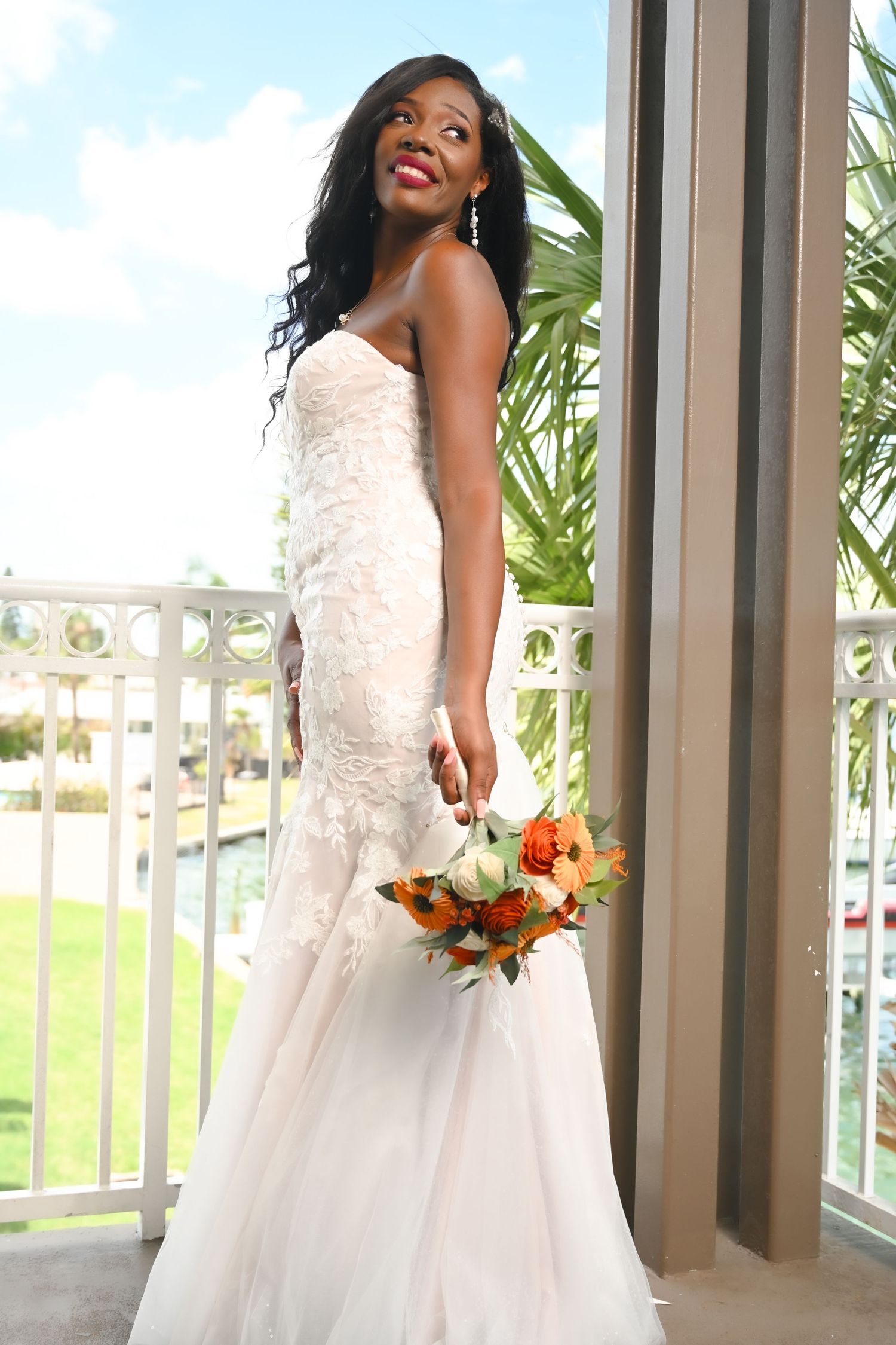 Bridal portraits in white lace dress holding orange and white bouquet.