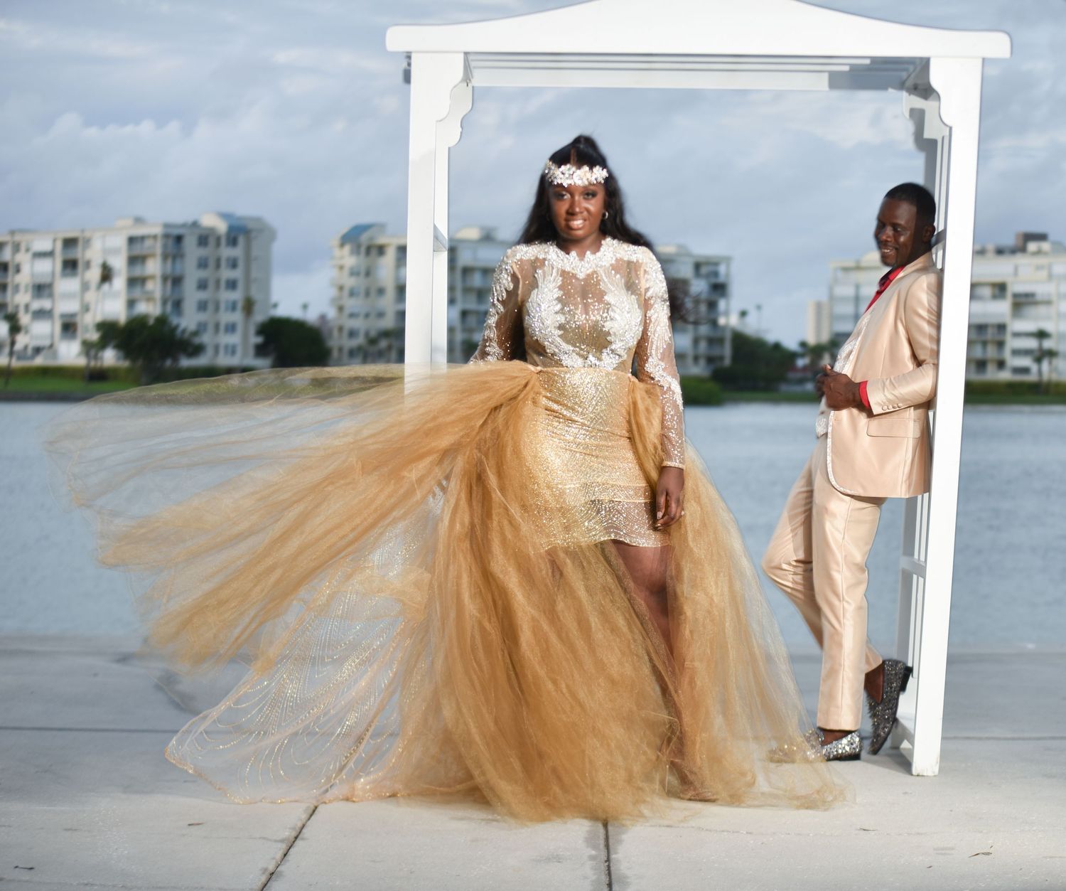 Bride in flowing champagne tulle gown poses by waterfront with dramatic dress movement.