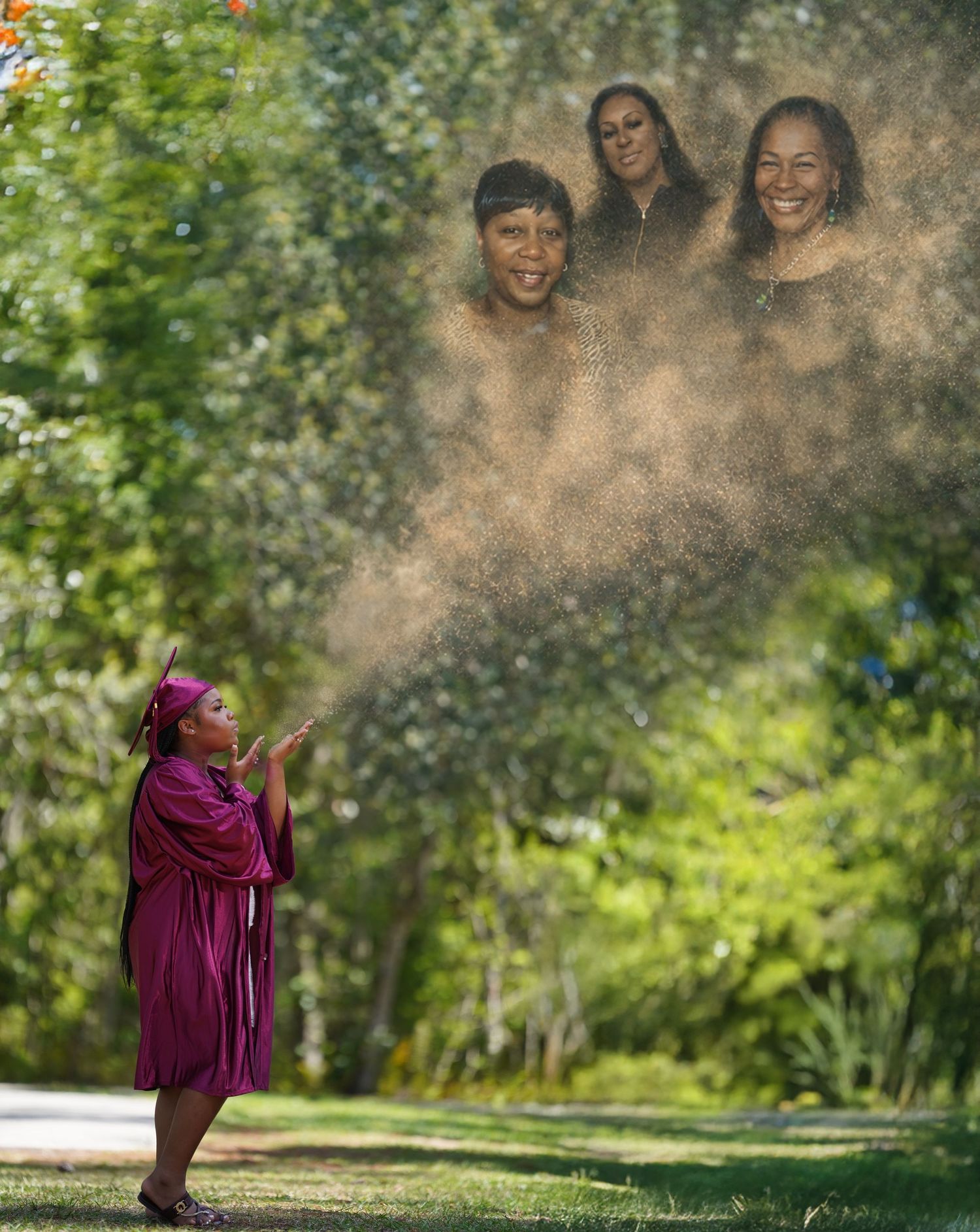 Graduate in magenta gown blows dust creating magical apparition of three smiling women in outdoor park setting.