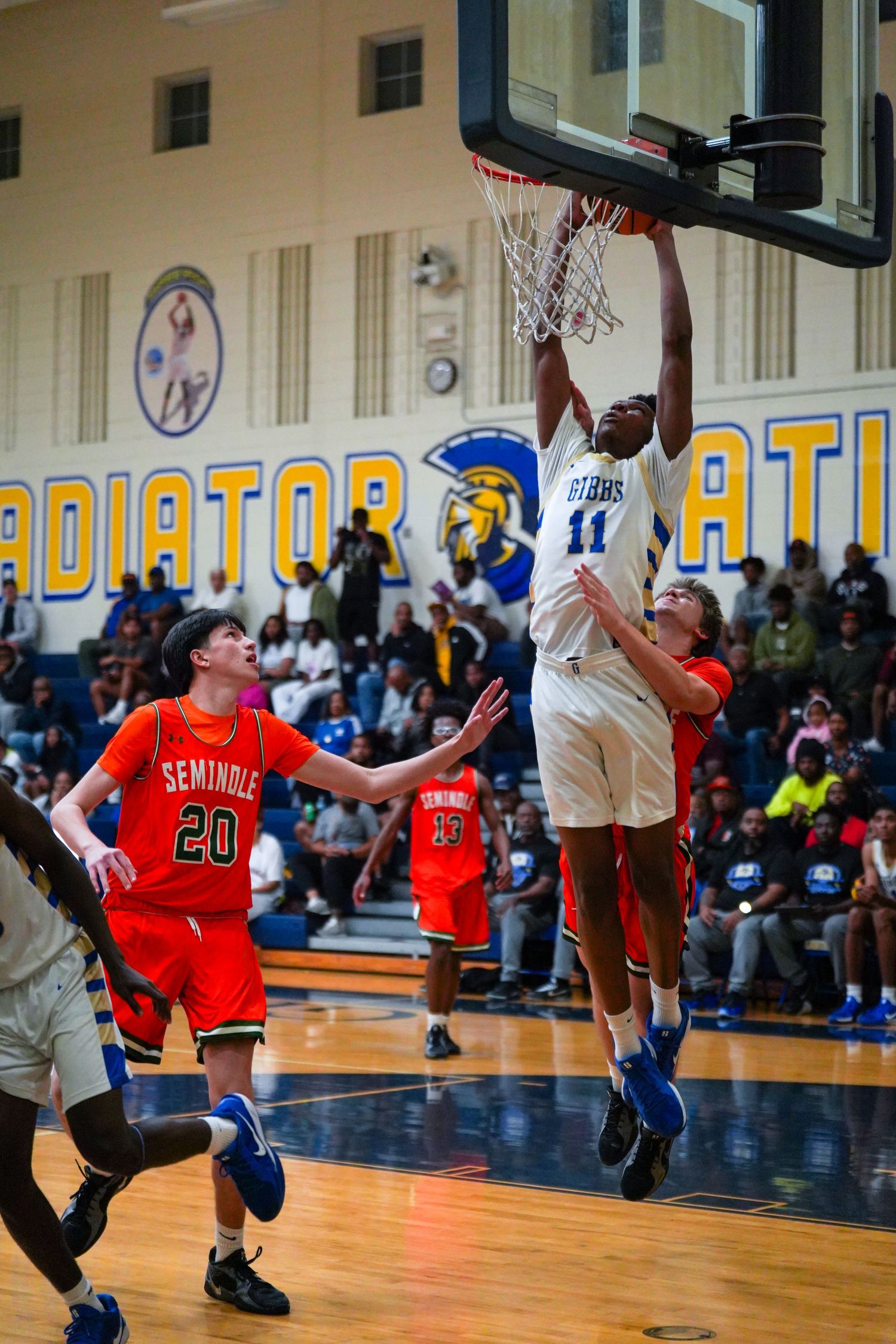 Player #11 in blue dunks over Seminole #20 in orange during a high school basketball game.
