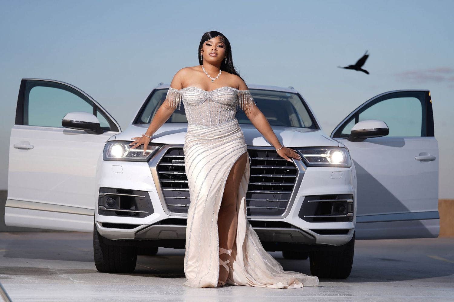 Elegant white car photoshoot with flowing dress and dramatic lighting against a light background.