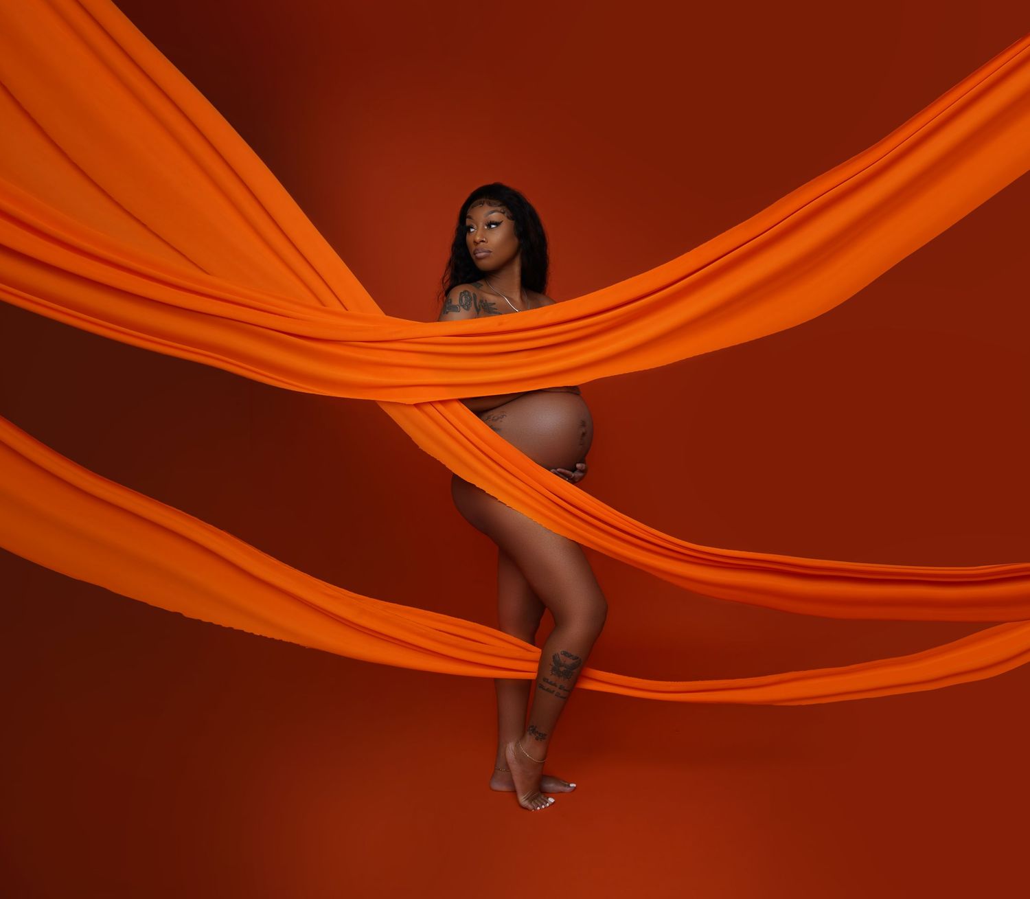 Artistic portrait series with flowing orange fabric creating dramatic movement and shapes against dark background.
