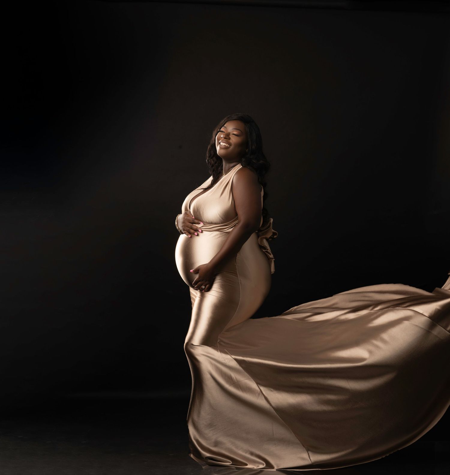 Elegant maternity portrait with flowing champagne fabric in dramatic studio lighting.