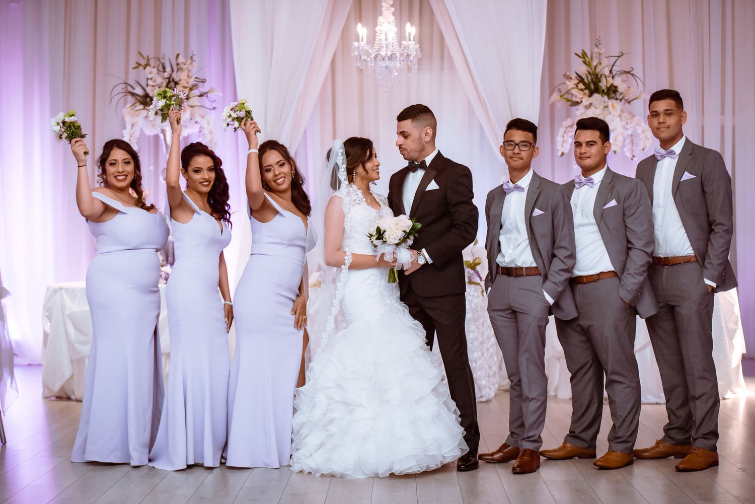 Wedding party in elegant attire poses together with bridesmaids in light blue dresses and groomsmen in gray suits.