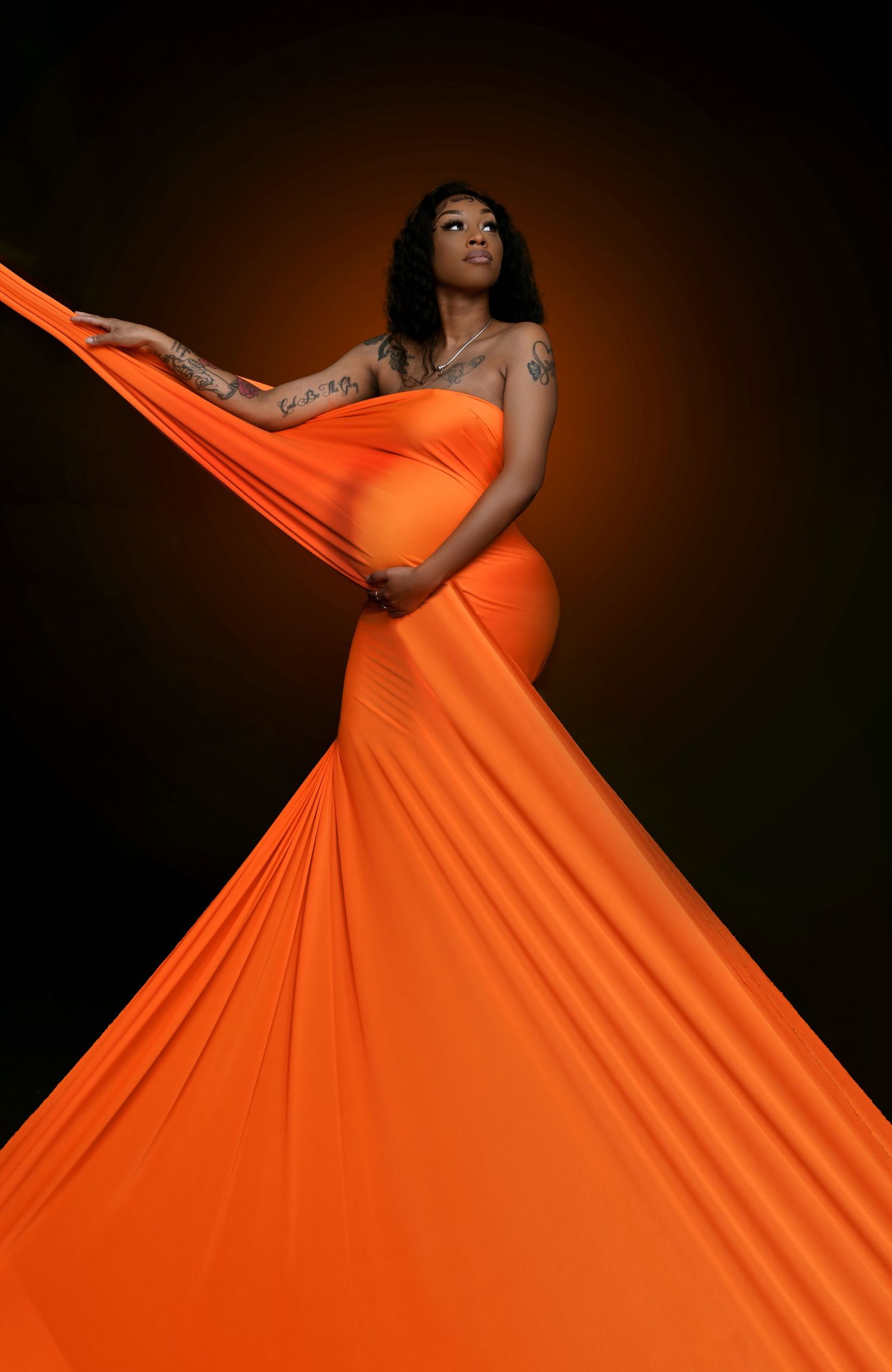 Flowing orange dress creates dramatic silhouette against dark background in fashion photography.