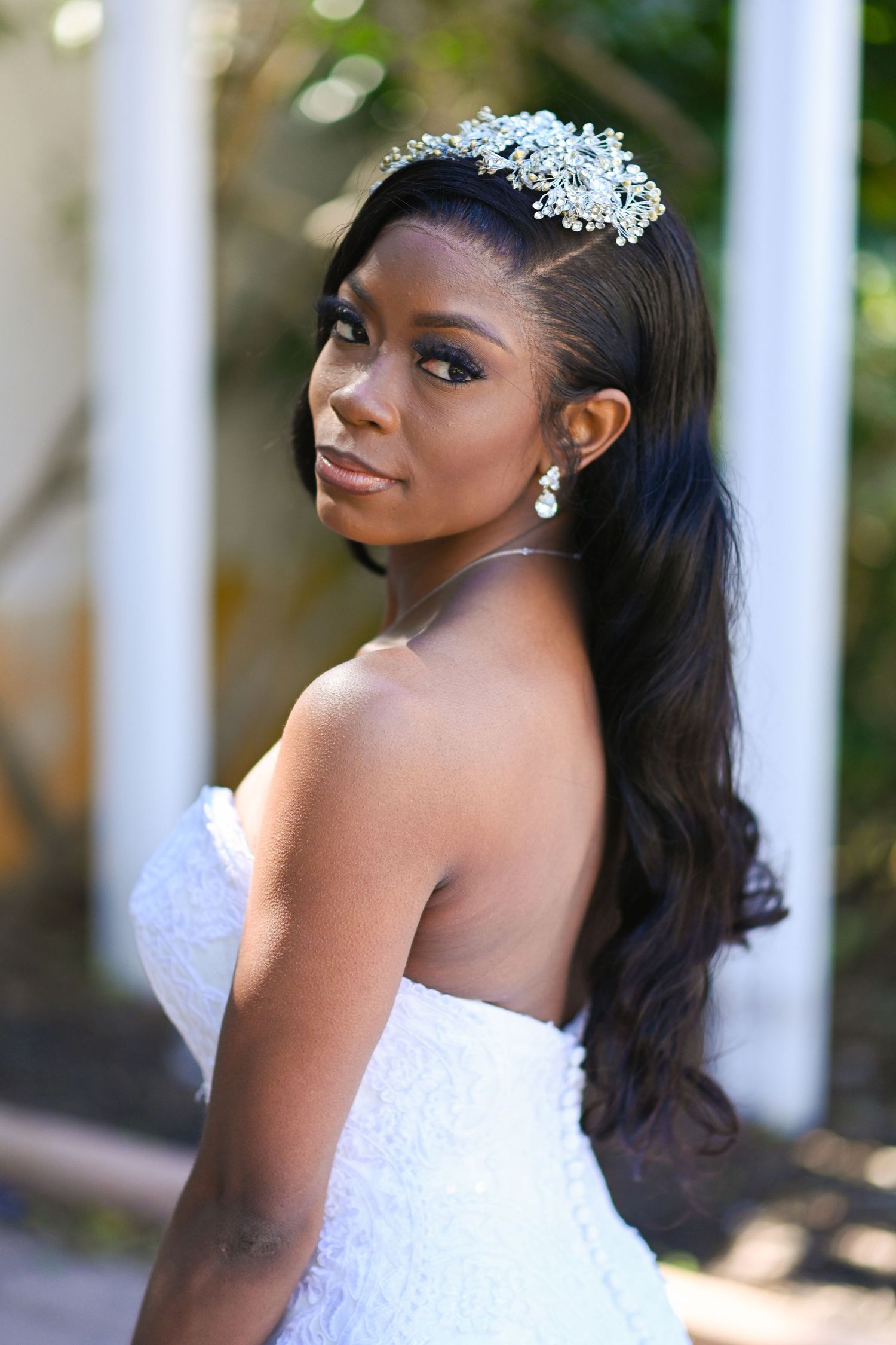 A beautiful Black bride in a strapless white gown wearing a crystal tiara and drop earrings, with long wavy hair.