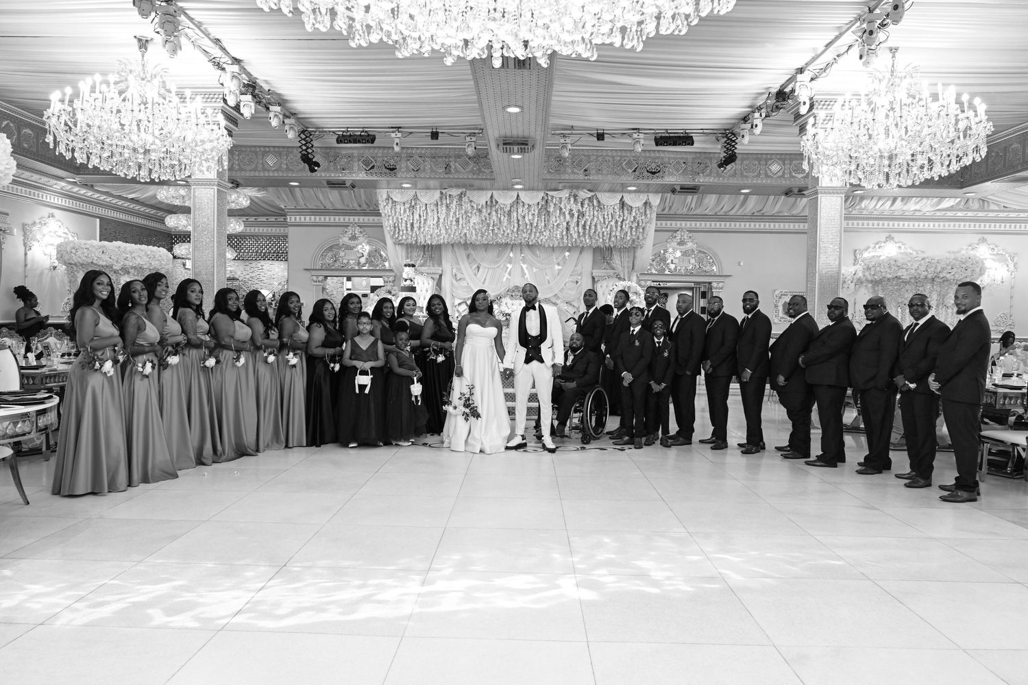Panoramic view of an elegant ballroom with crystal chandeliers and wedding guests lined up along the walls.