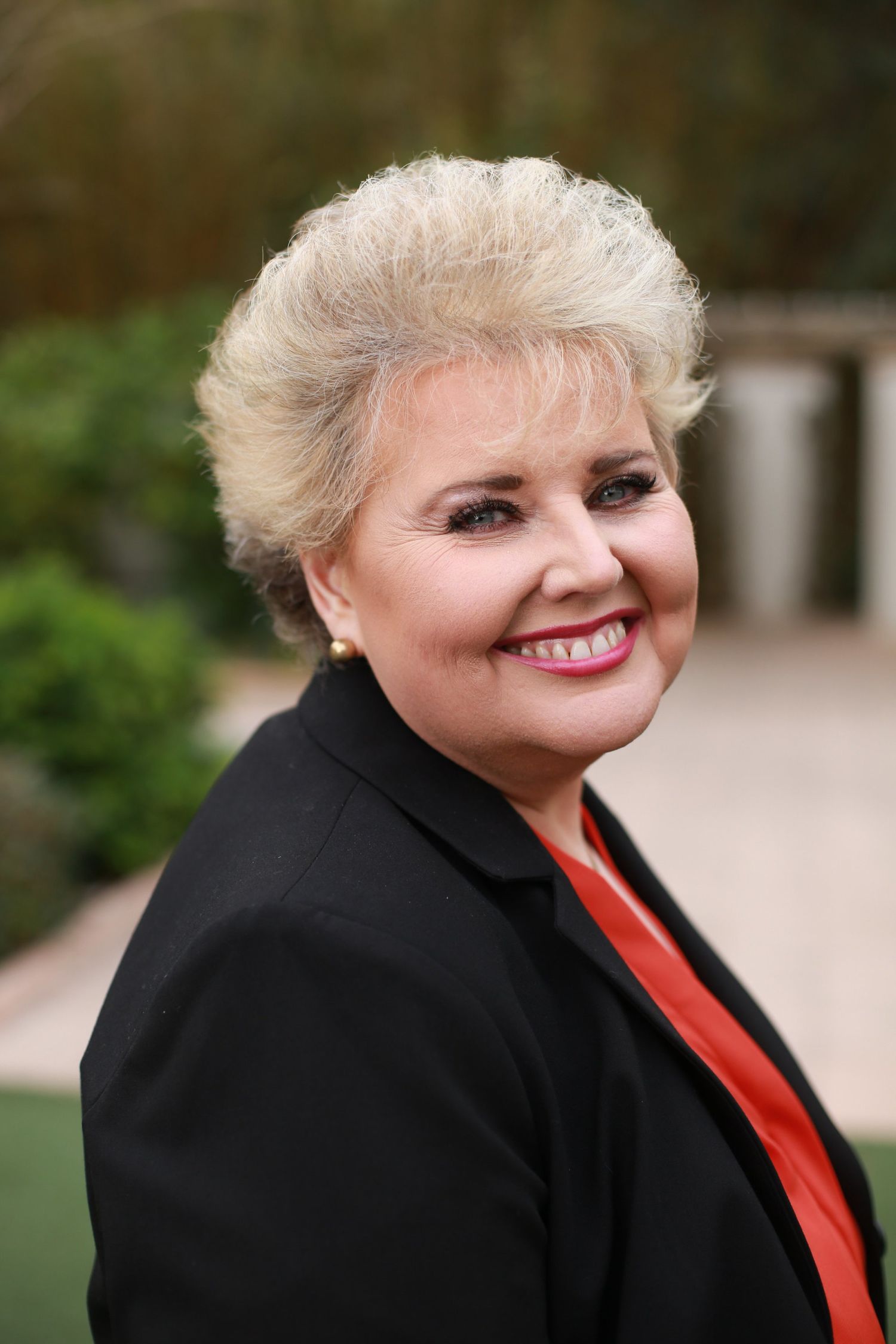 A series of headshots showing someone with platinum blonde hair wearing a black blazer and red scarf against a blurred background.