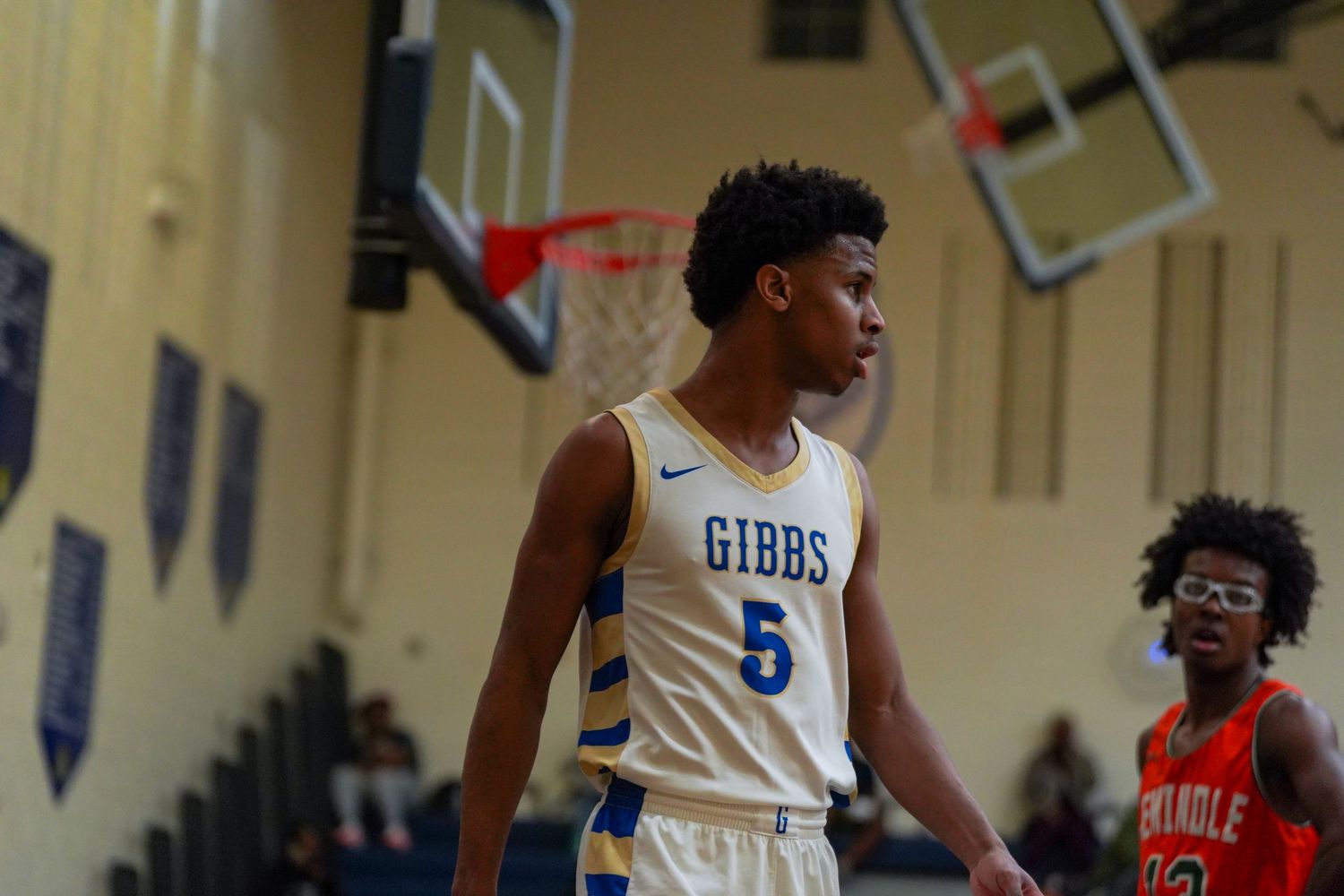 Gibbs #5 basketball player stands on court during a high school game in a blue and gold Nike uniform.