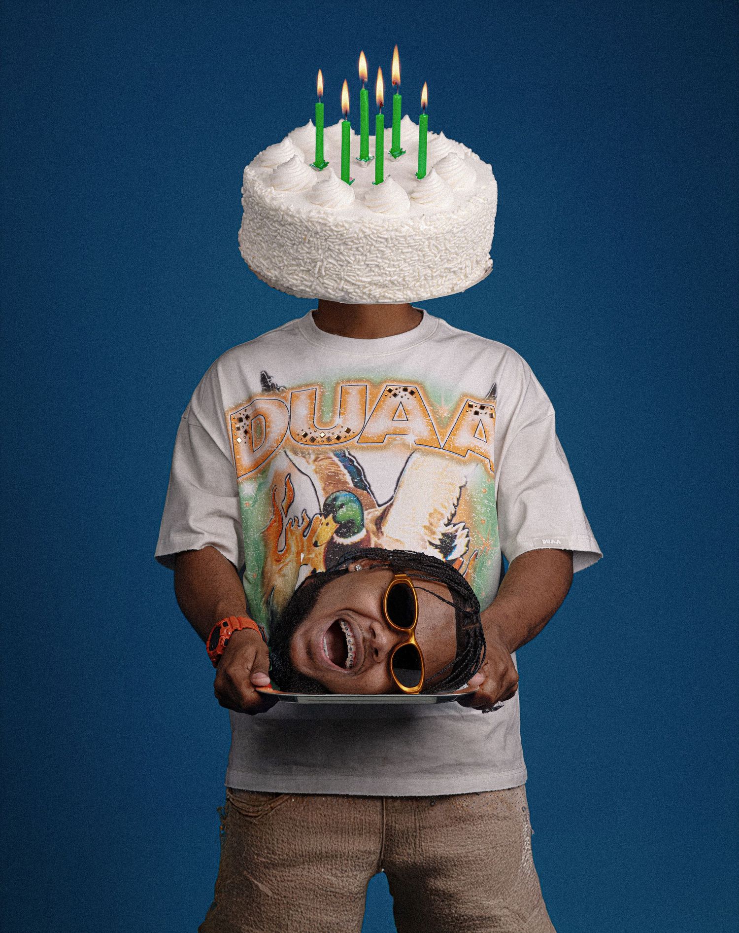 Person wearing graphic tee holds a platter with a face print, birthday cake with green candles balanced on their head.