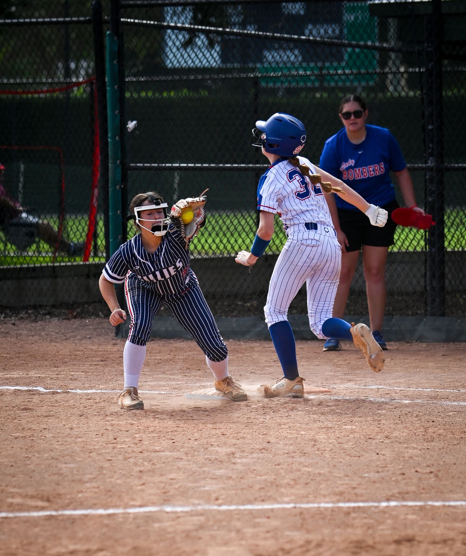 Youth softball players in action near home plate during a competitive game on a sunny day.