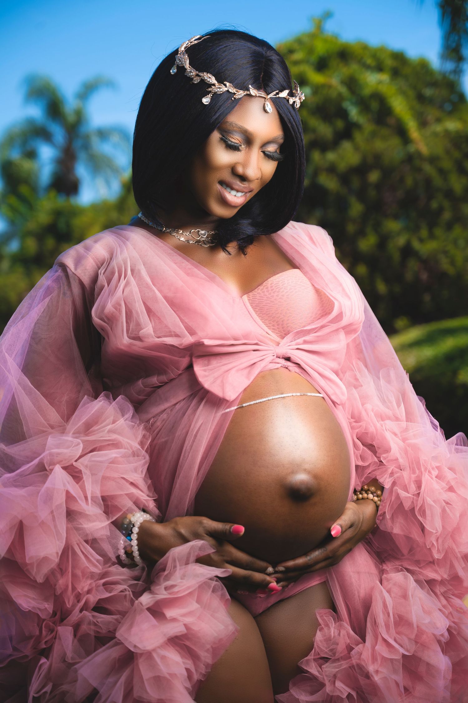 Outdoor maternity photoshoot featuring pink tulle gown against tropical greenery.