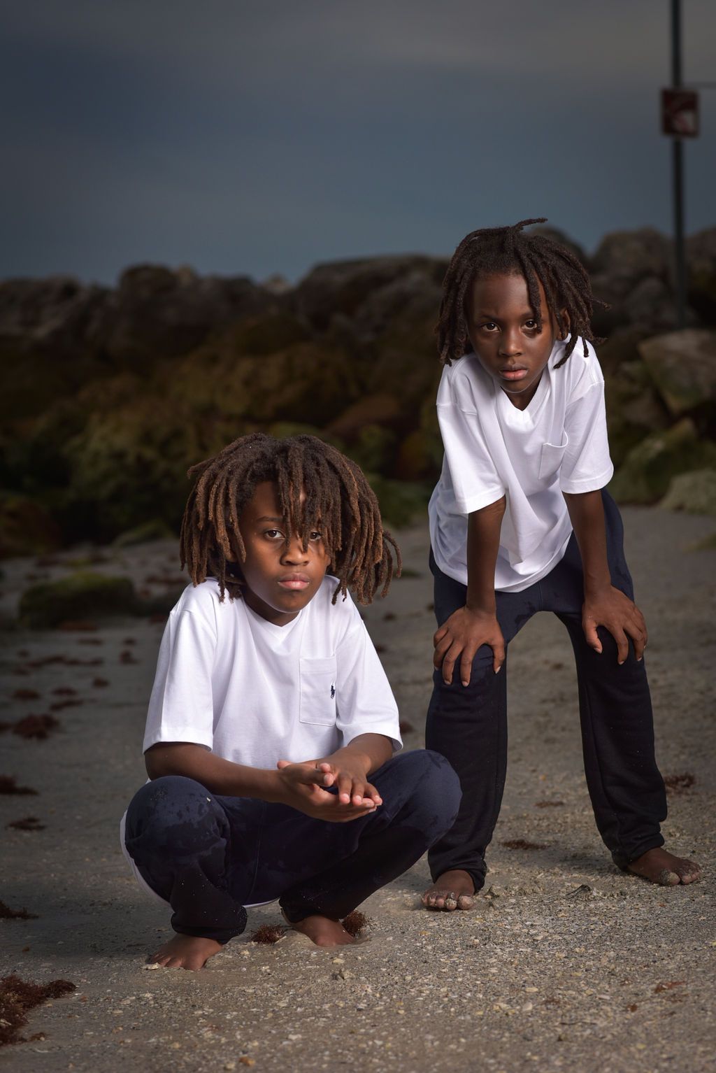 Artistic portrait series of youth in white shirts and dark pants crouching on rocky ground on Clearwater Beach Florida.