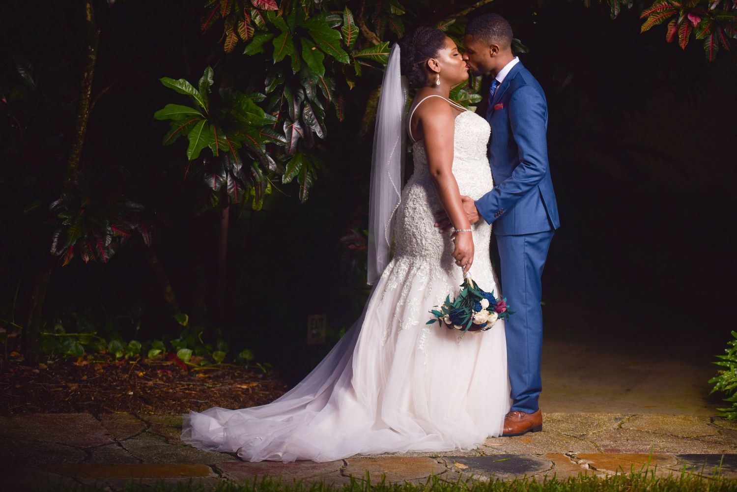 Bride and groom sharing a kiss at night, bride in white mermaid gown with veil, groom in blue suit.