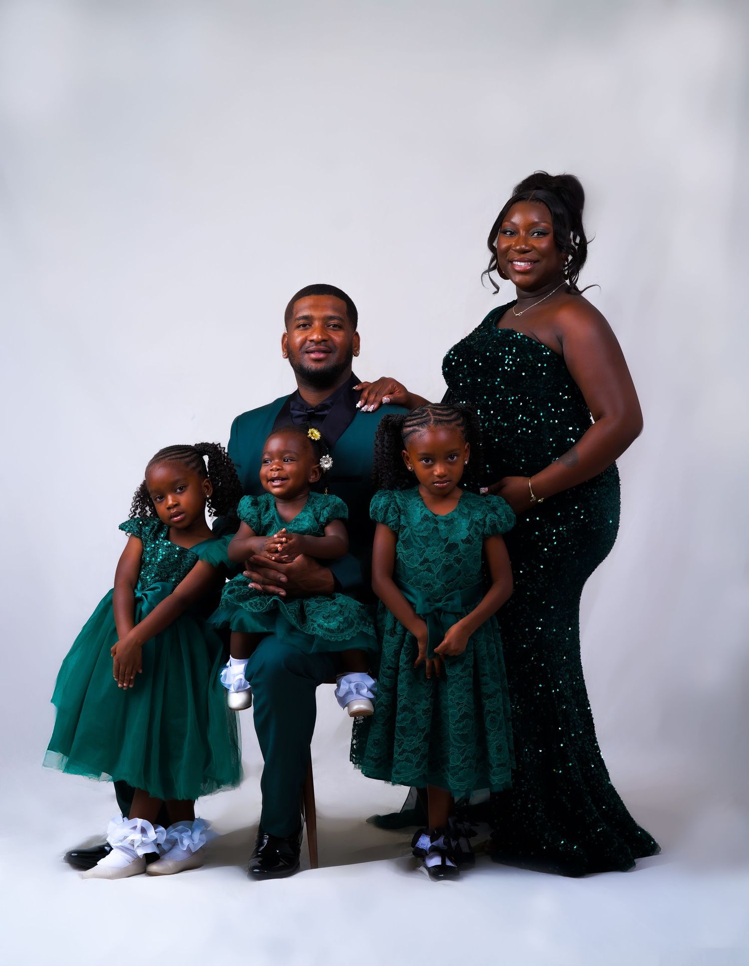 A joyful family of five in matching emerald green outfits poses together for a professional studio portrait photo.