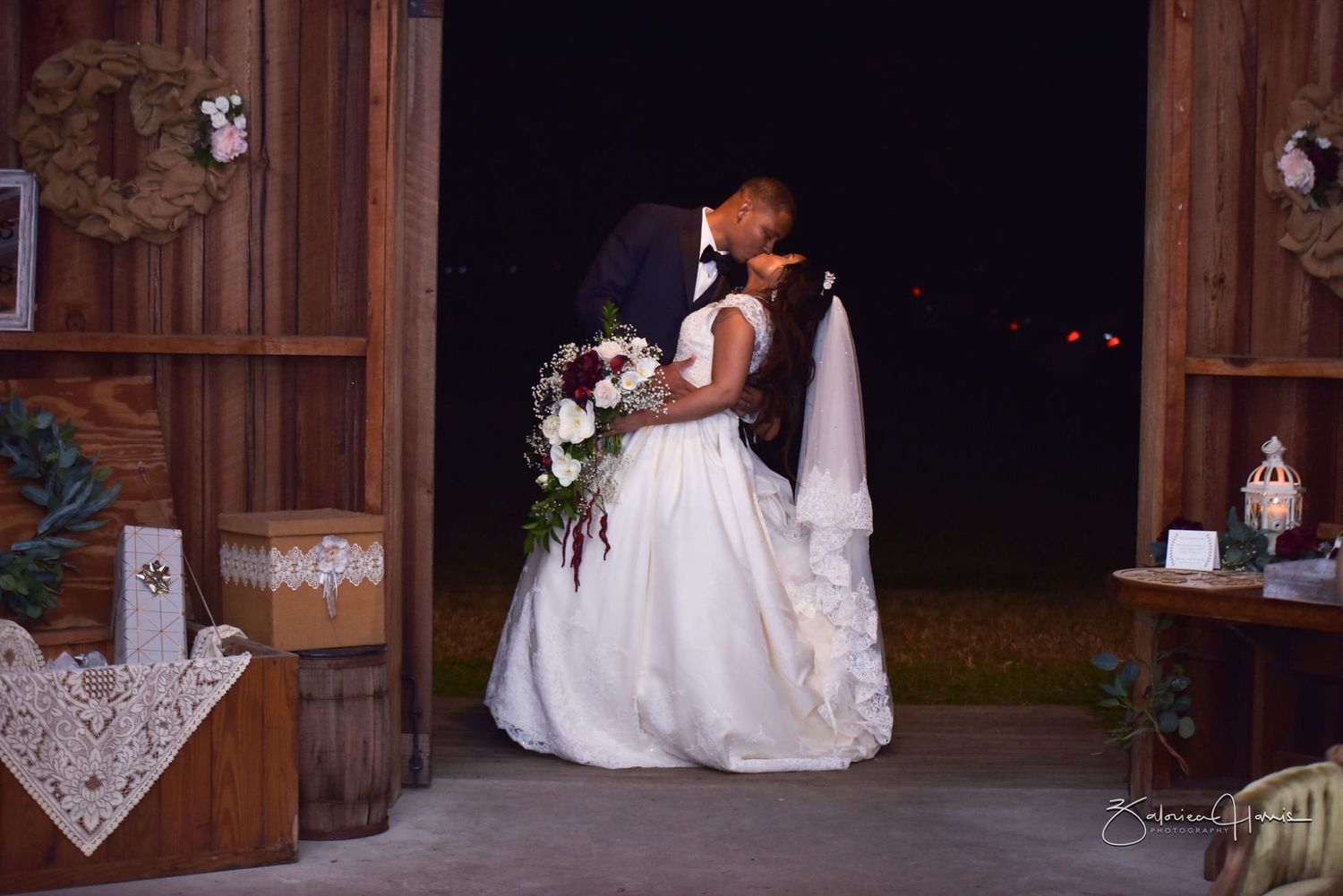 A wedding couple shares a romantic kiss during their reception in a rustic barn venue with wooden details.