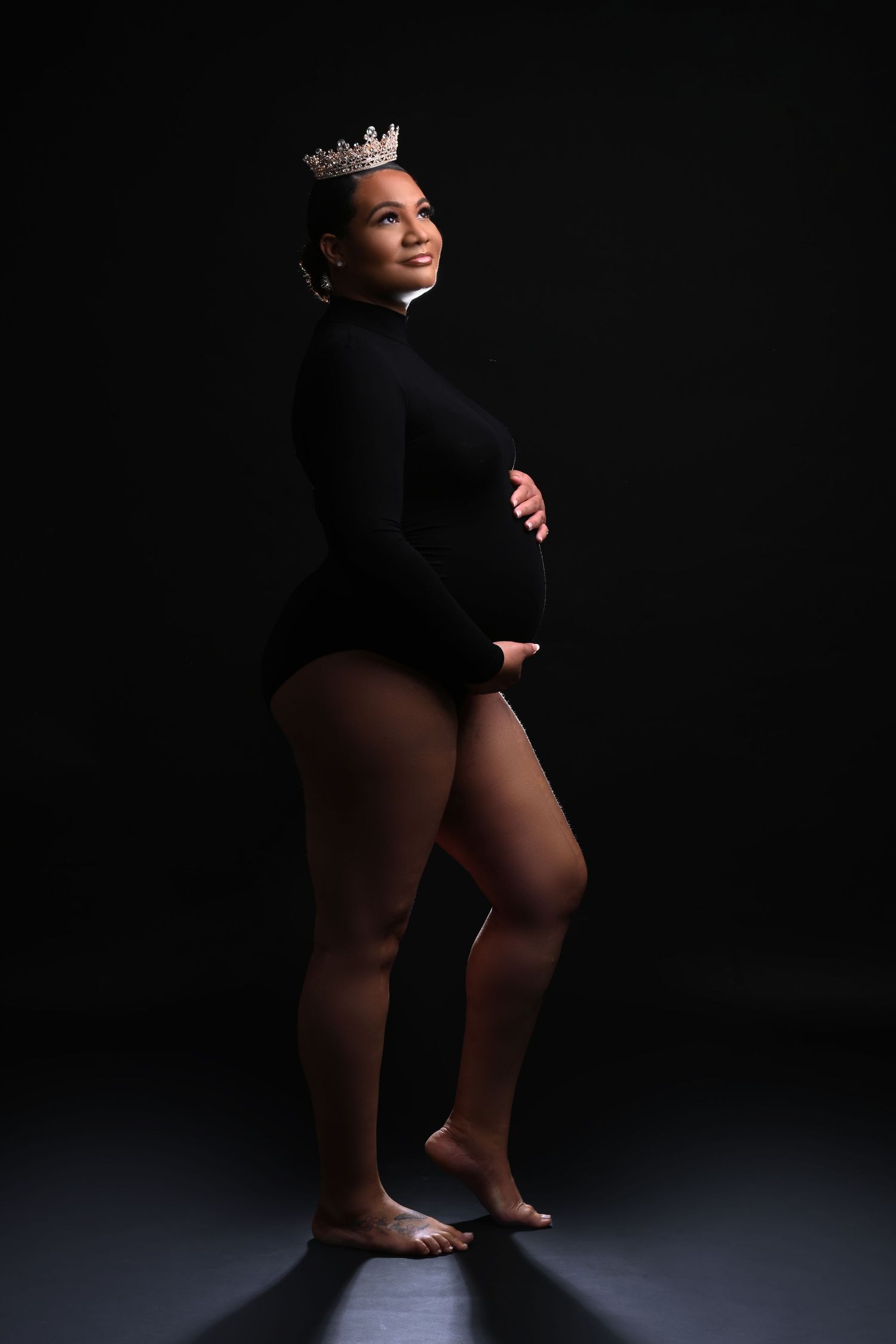 Dramatic silhouette maternity portraits in black outfit against dark background.