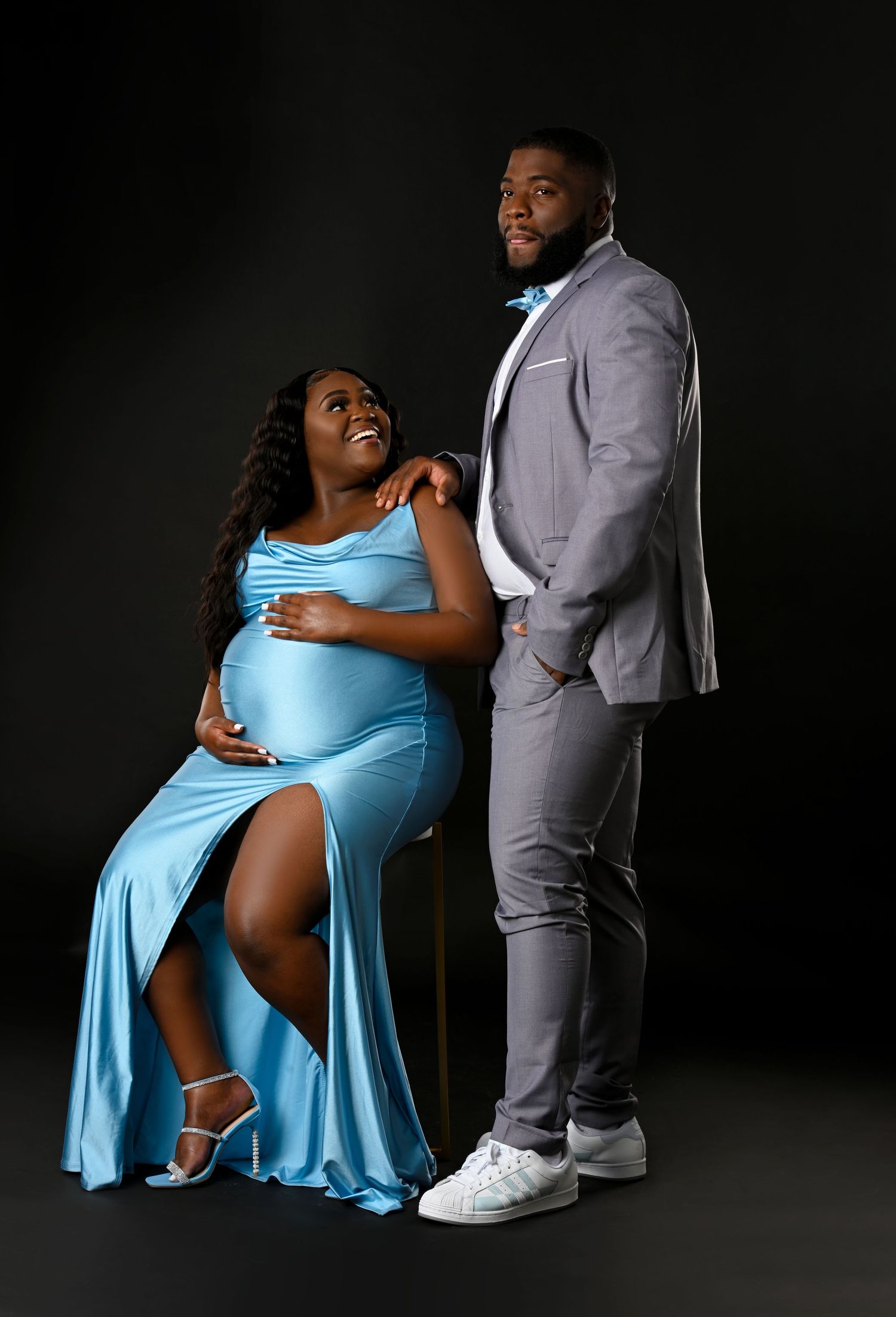 Couple's maternity photoshoot with person in light blue dress and partner in grey suit.