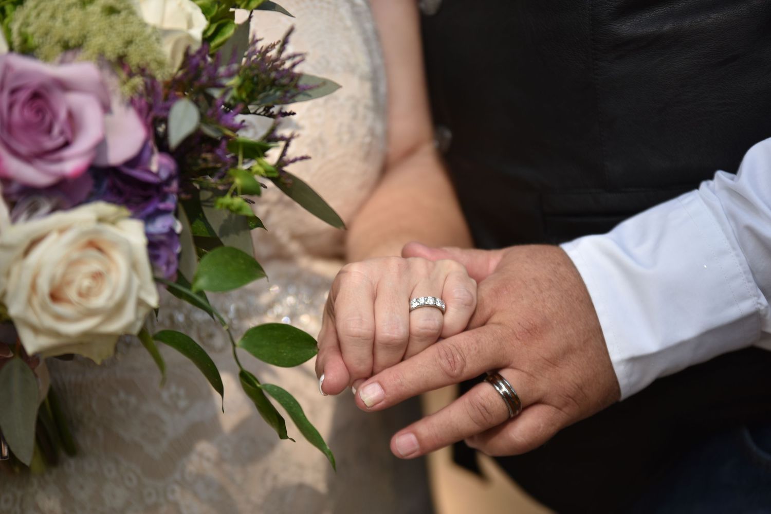 Close-up of wedding rings and purple floral bouquet details.