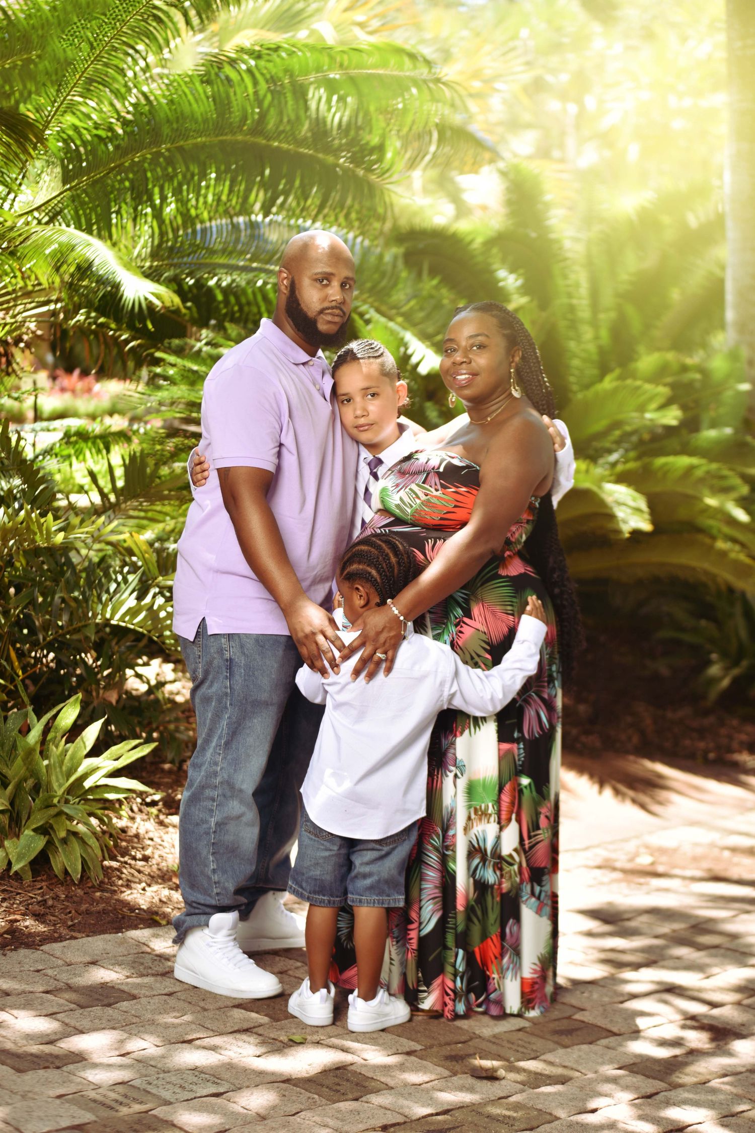 A happy family of four poses together in a lush tropical garden, with warm sunlight filtering through green palm trees.