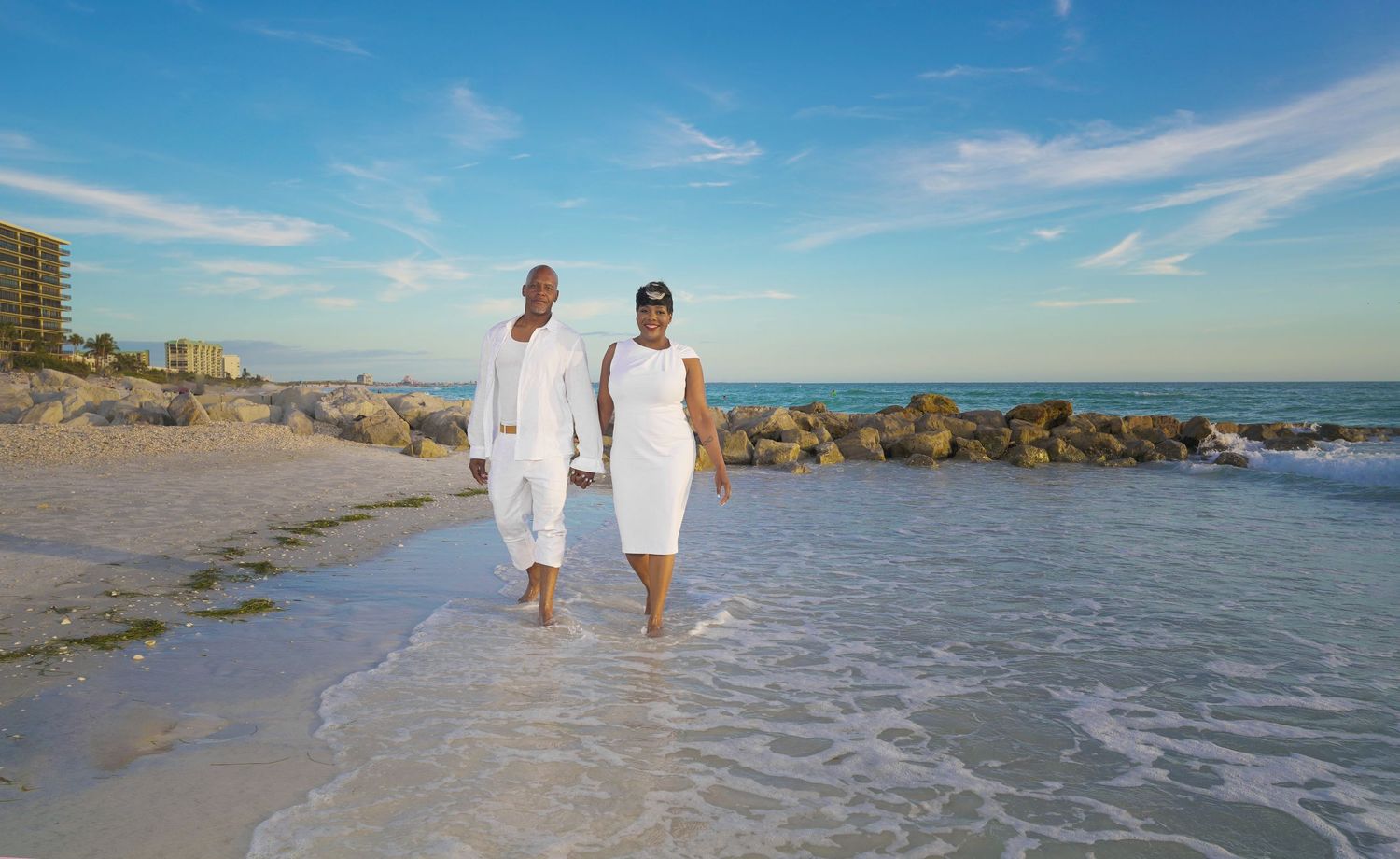Couple walking together on beach shoreline wearing white outfits in Saint Petersburg Florida.