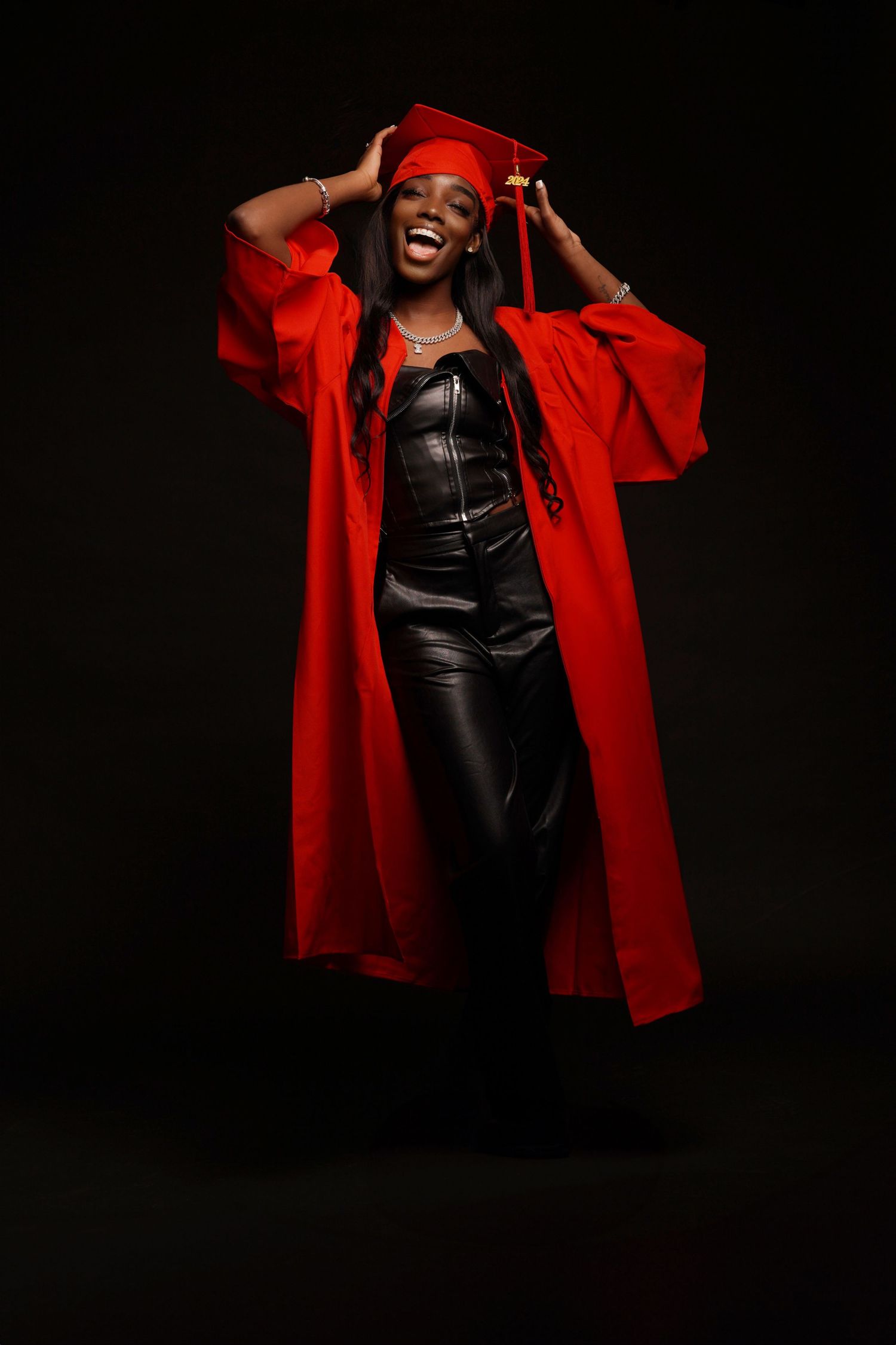 Fashion graduate portrait in red coat and black leather outfit against dark background with dramatic lighting in Saint Petersburg Florida.