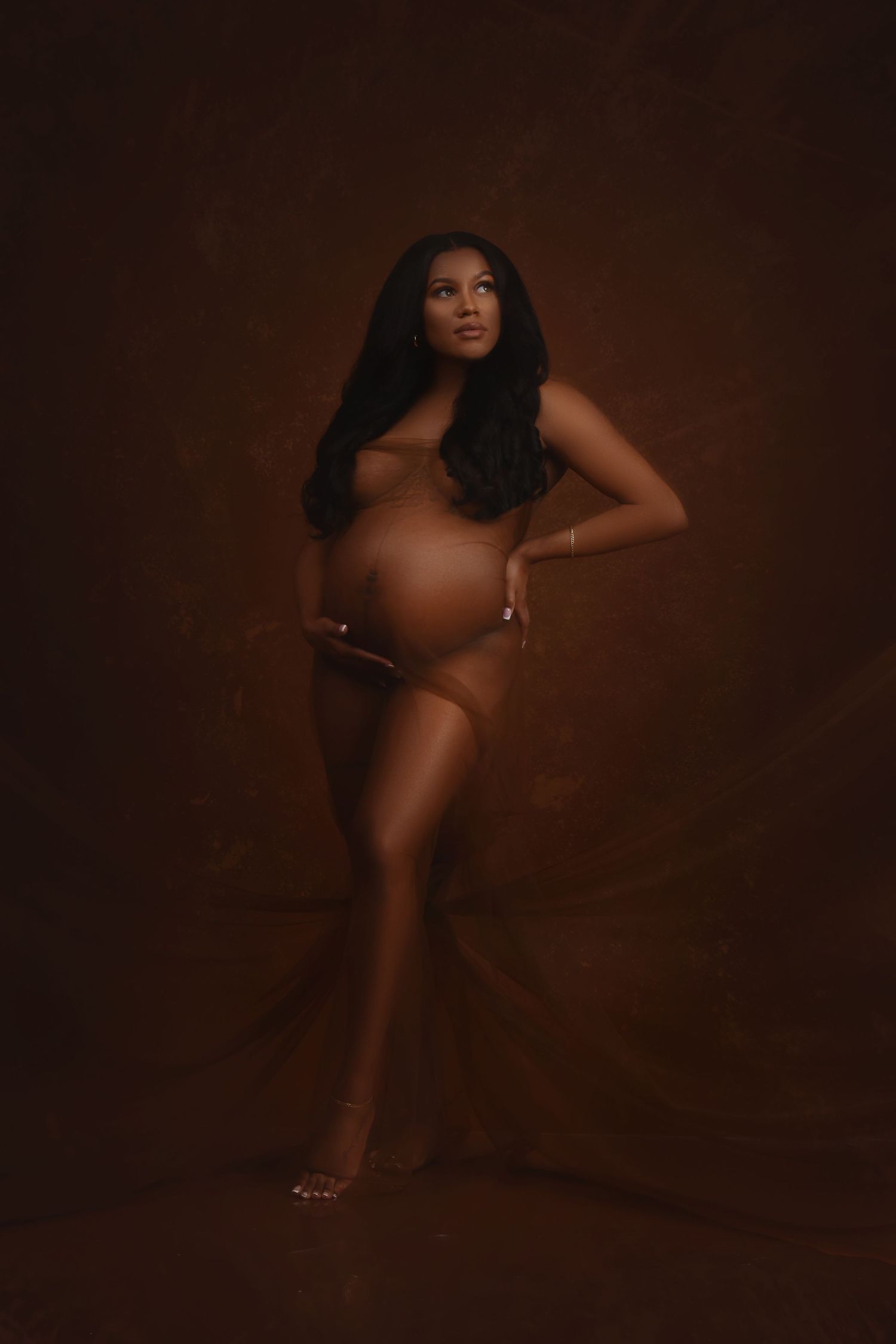 Artistic maternity photoshoot with moody dark lighting and dramatic poses.