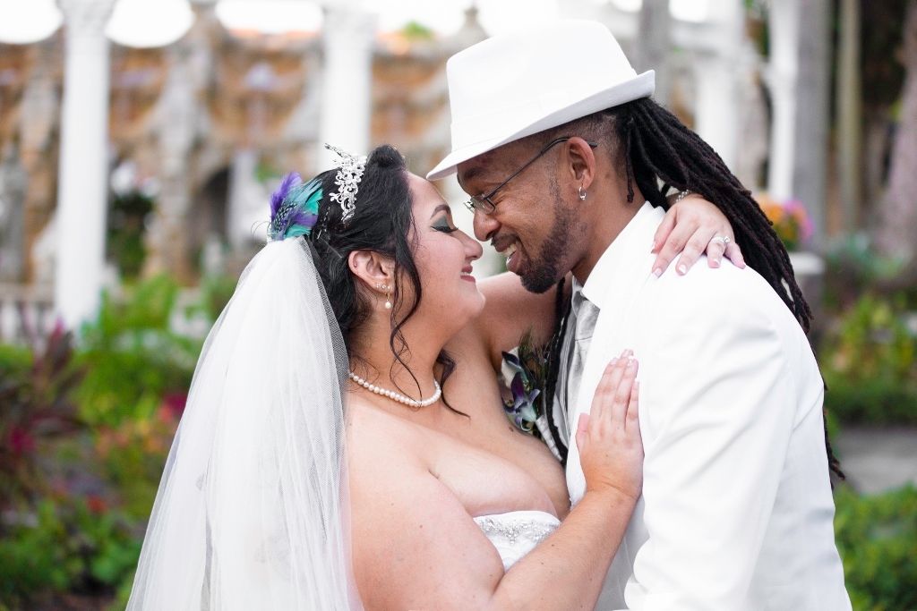 A romantic wedding couple shares an intimate moment under a veil in an outdoor garden setting.