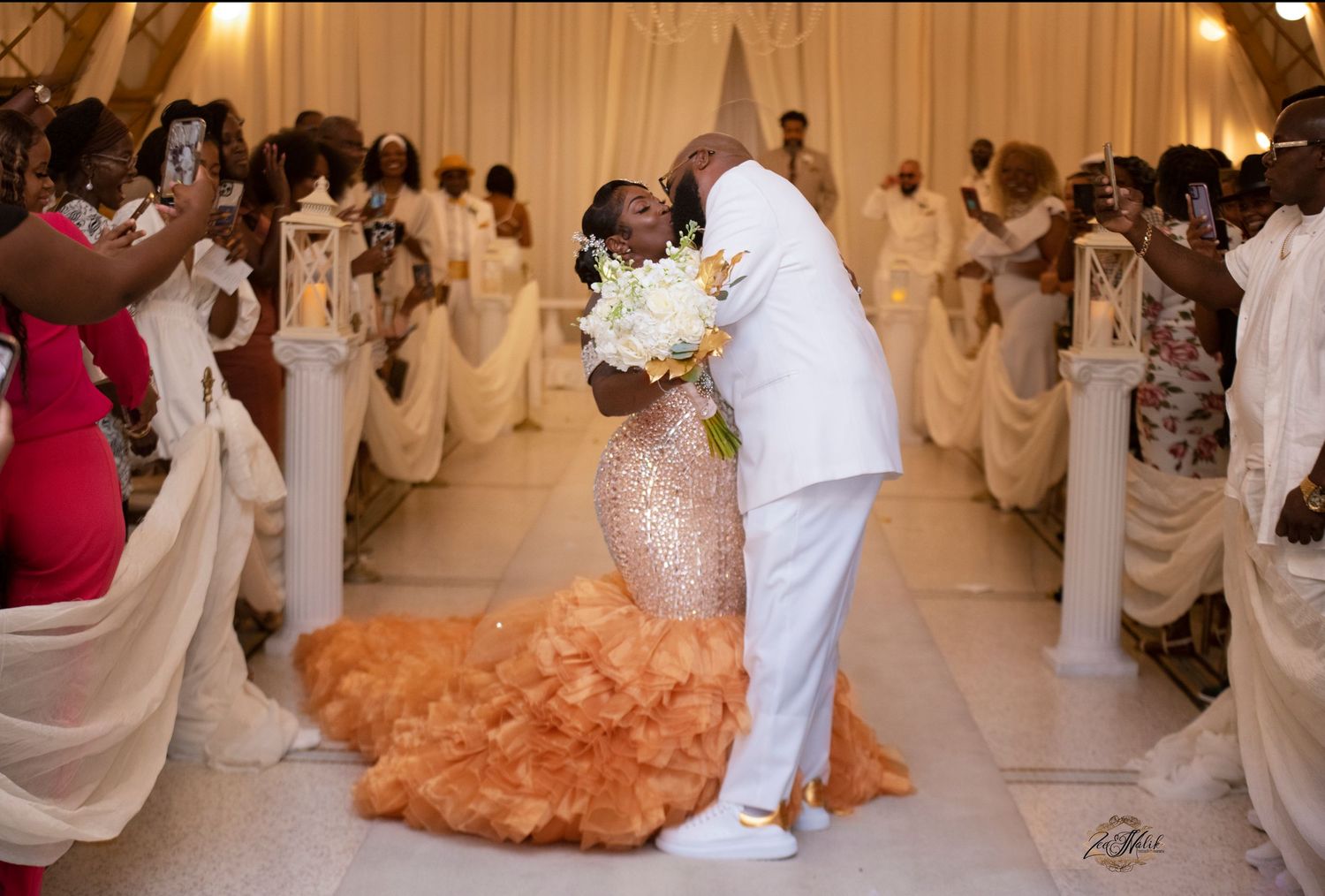 A wedding ceremony scene with guests in white attire standing in an elegant indoor venue.