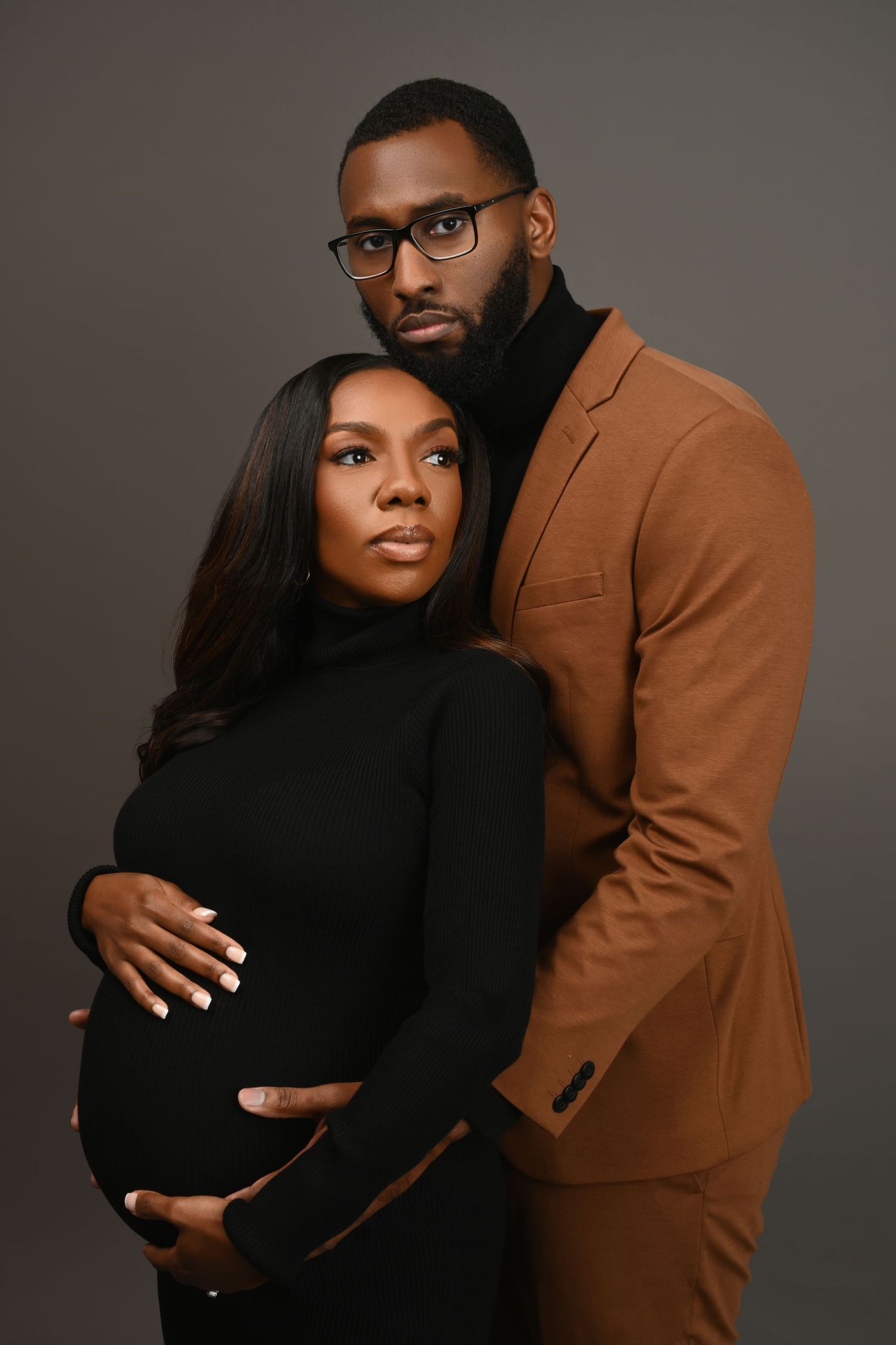 Intimate maternity studio portraits with couple in black dress and brown blazer.