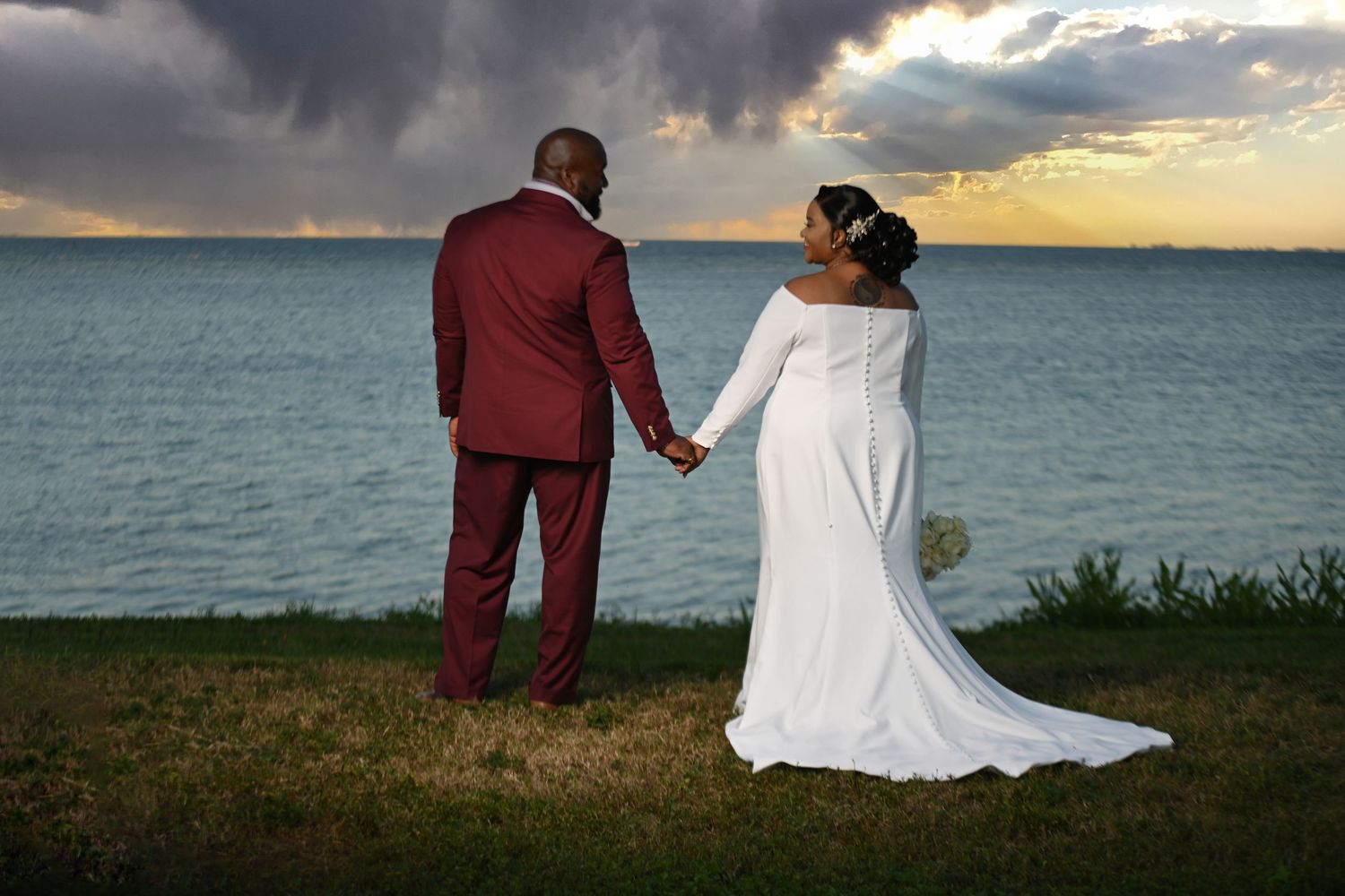 Panoramic view of wedding couple walking along oceanfront at golden hour.