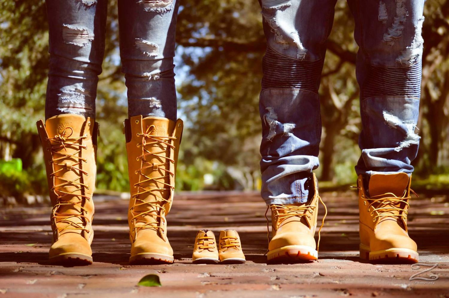 Family wearing matching tan work boots stands together on wooden deck with baby shoes in the middle.
