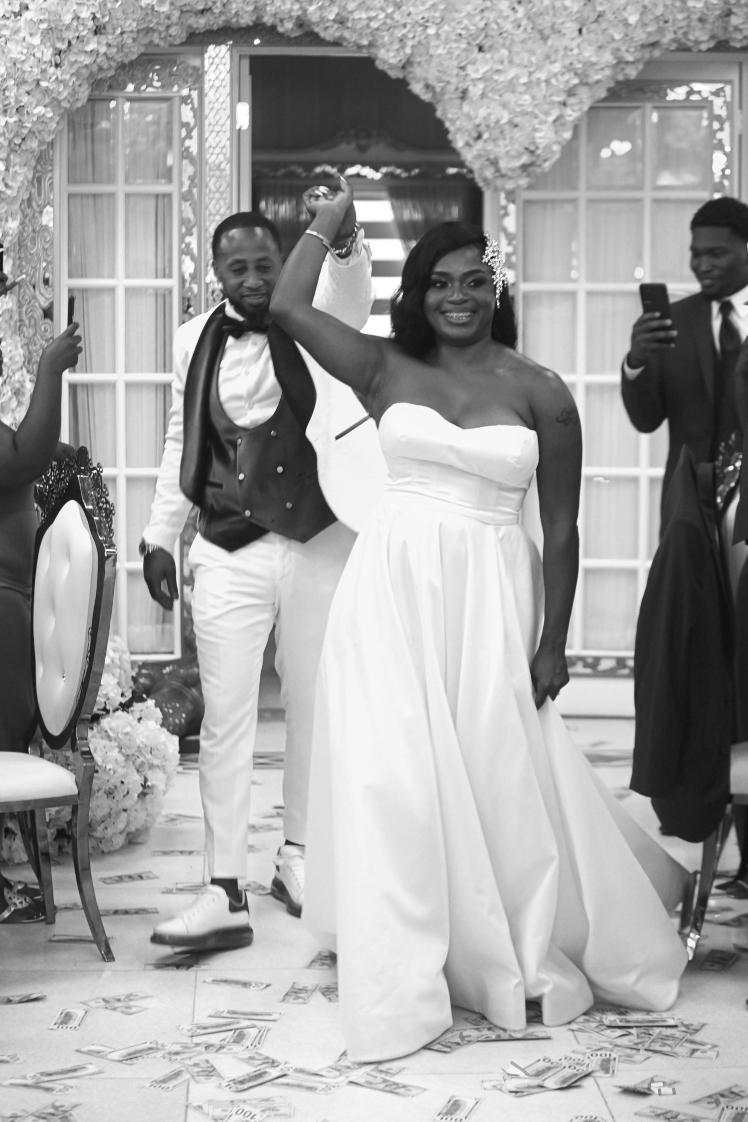 Black and white photo of a joyful bride in a strapless gown raising her fist while groom celebrates at their wedding.