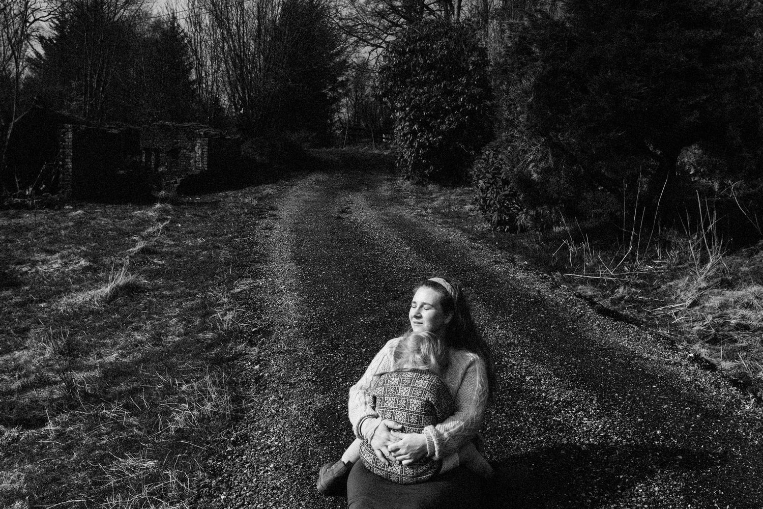 A black and white photo capturing a tender moment on a wooded path.