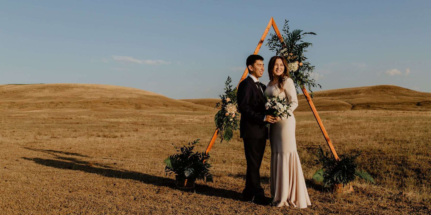 Panoramic view of rolling golden hills under blue sky with scattered trees and a couple in the distance.