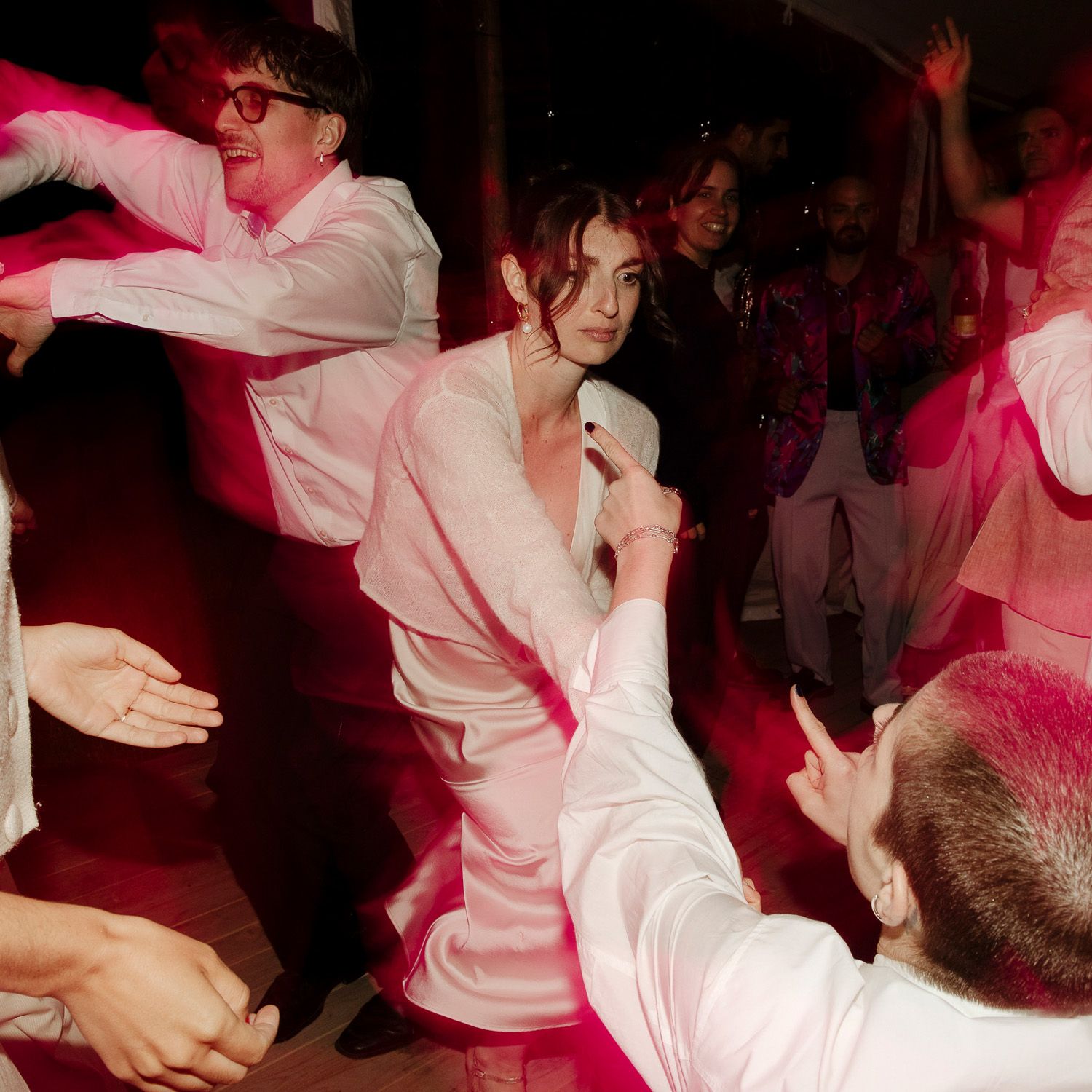 People dancing and celebrating at a party with red lighting and white outfits on a dance floor.