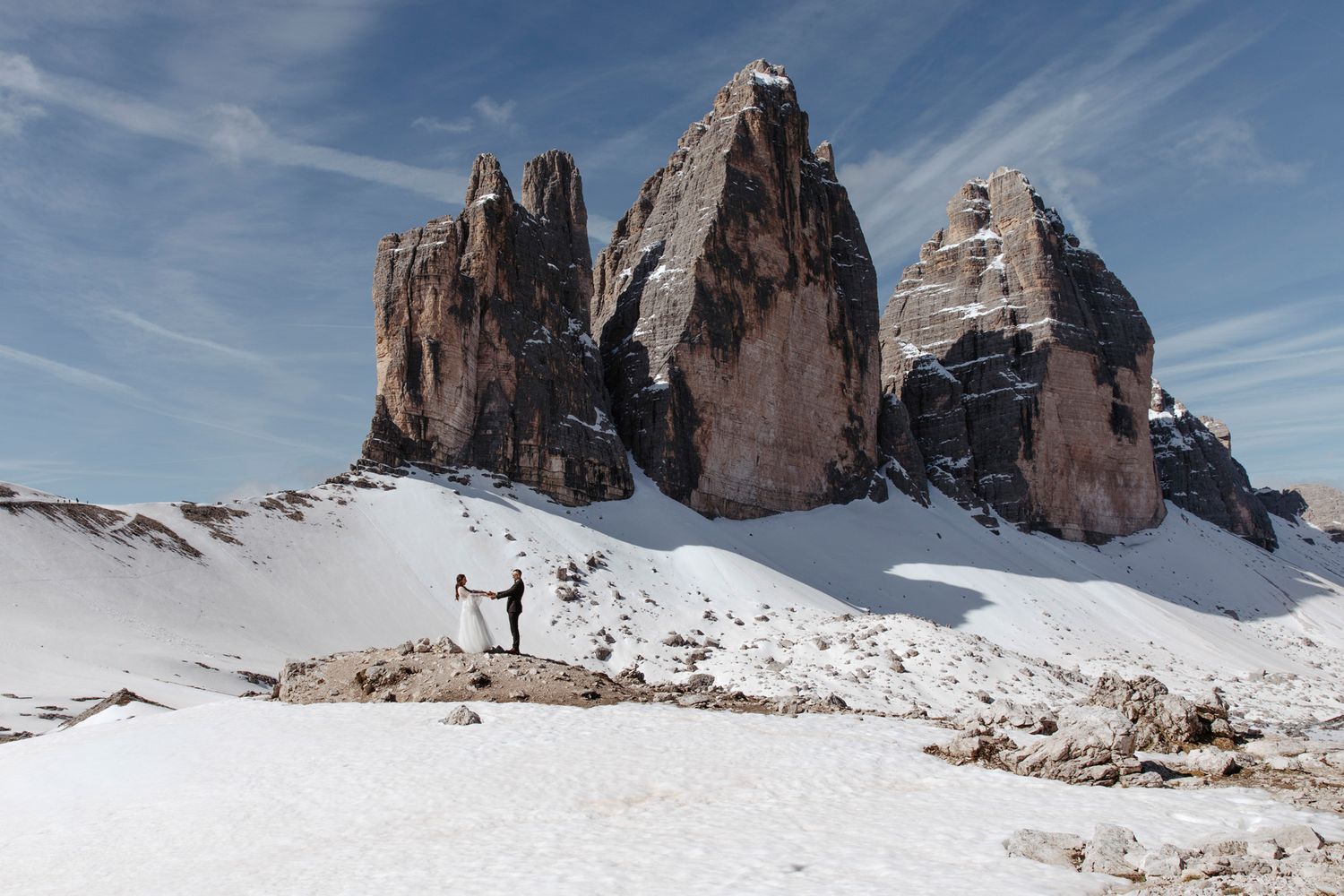 Wide panoramic view of snow-covered Dolomites mountains against blue sky.