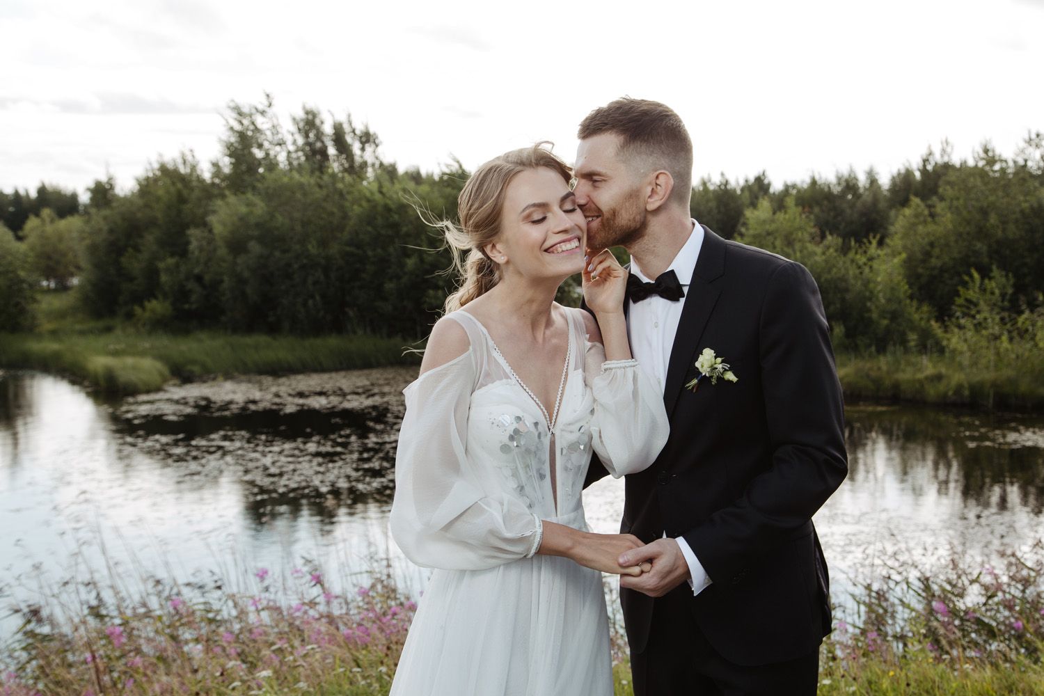 Romantic moment captured between couple in wedding attire by scenic lake.