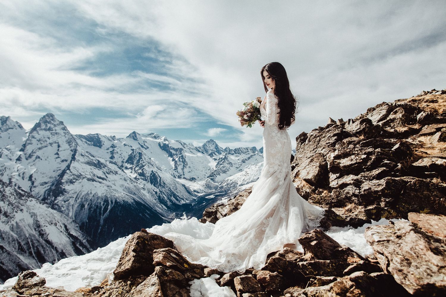 Snowy mountain peaks create dramatic backdrop for scenic wedding photography on rocky cliffs.