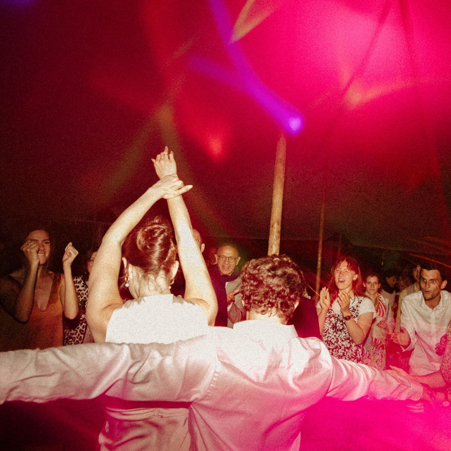 A group of people dancing and celebrating at a party with vibrant pink lighting and energetic atmosphere.