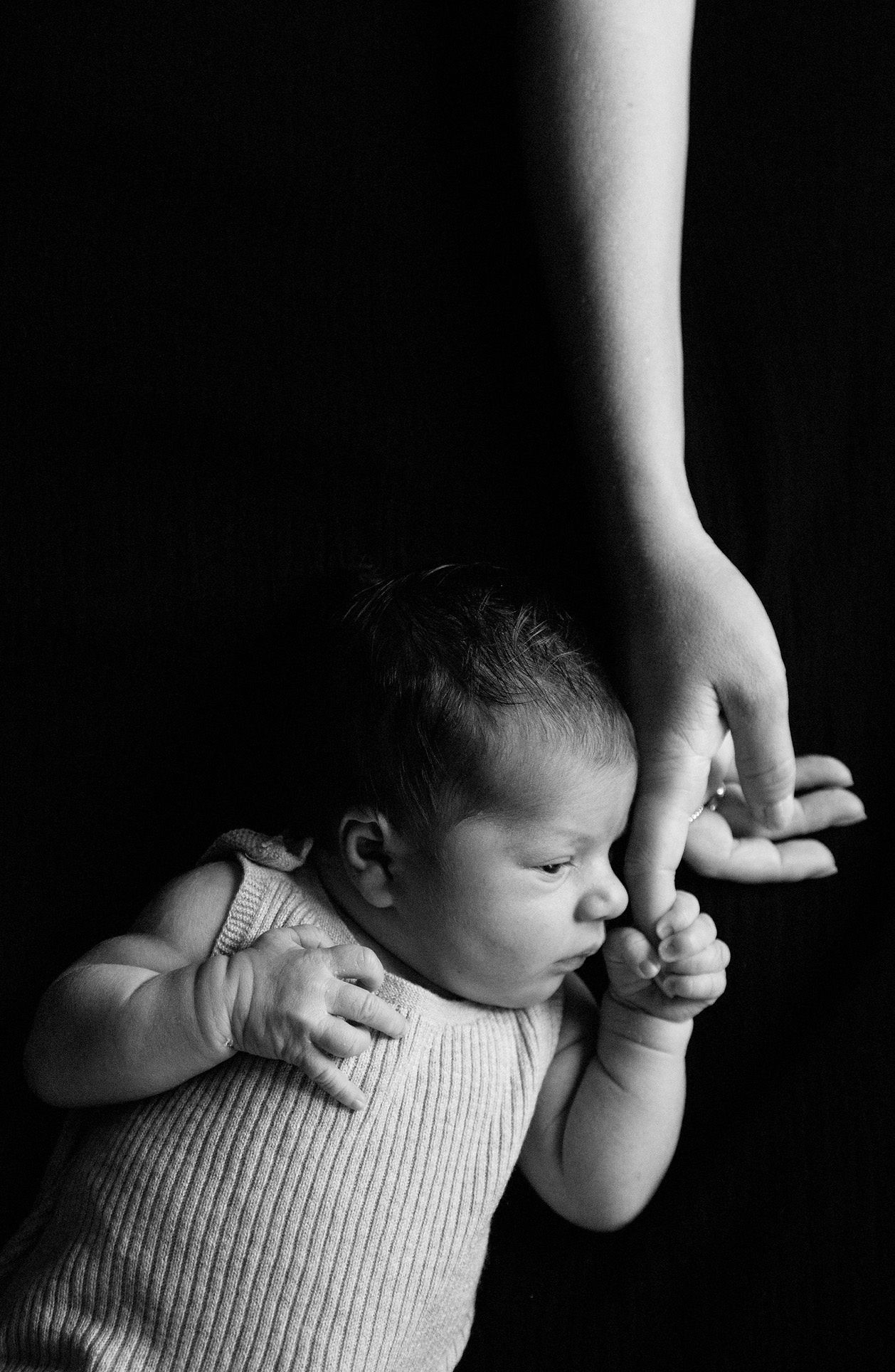 A series of black and white photos showing a baby lying down while a hand gently touches their head.