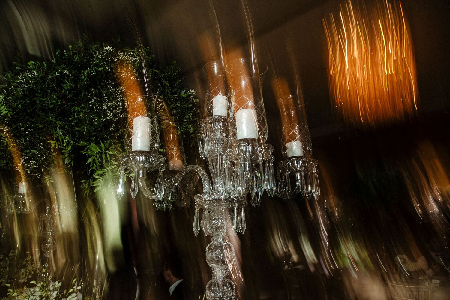 Crystal chandeliers adorned with greenery create an elegant wedding reception atmosphere in a rustic venue.