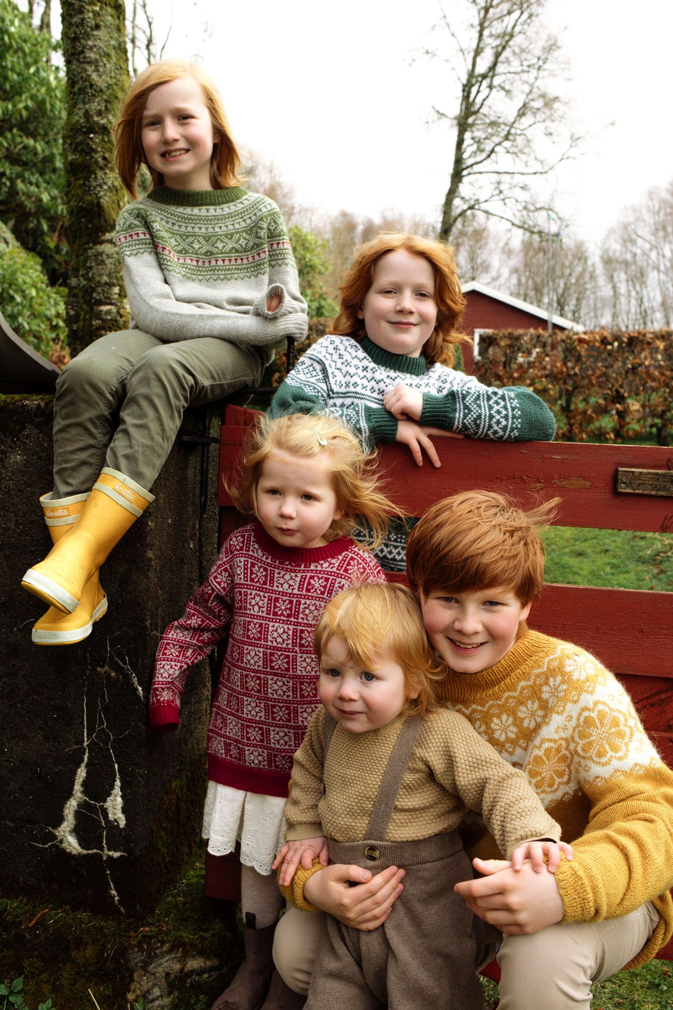 A group wearing cozy patterned sweaters pose together on a wooden bench in an outdoor setting.