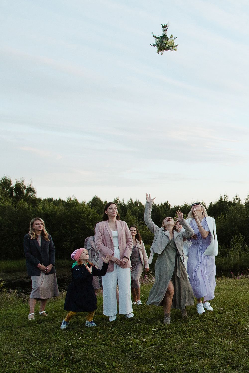 Wedding party poses playfully in a grassy field during golden hour.